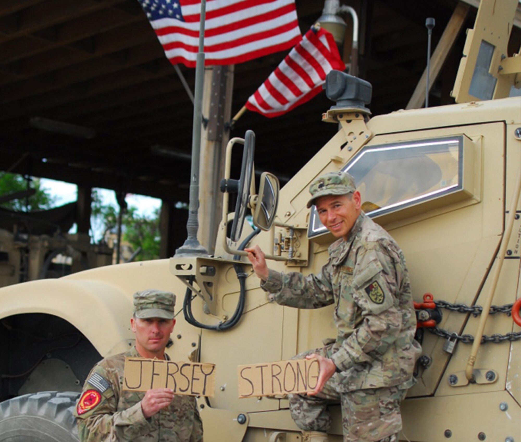 A picture of Lt. Col. Jesse Arnstein and Tech. Sgt. Chris Donohue posing for a photo in front of a military vehicle, holding a sign that says, "Jersey Strong".