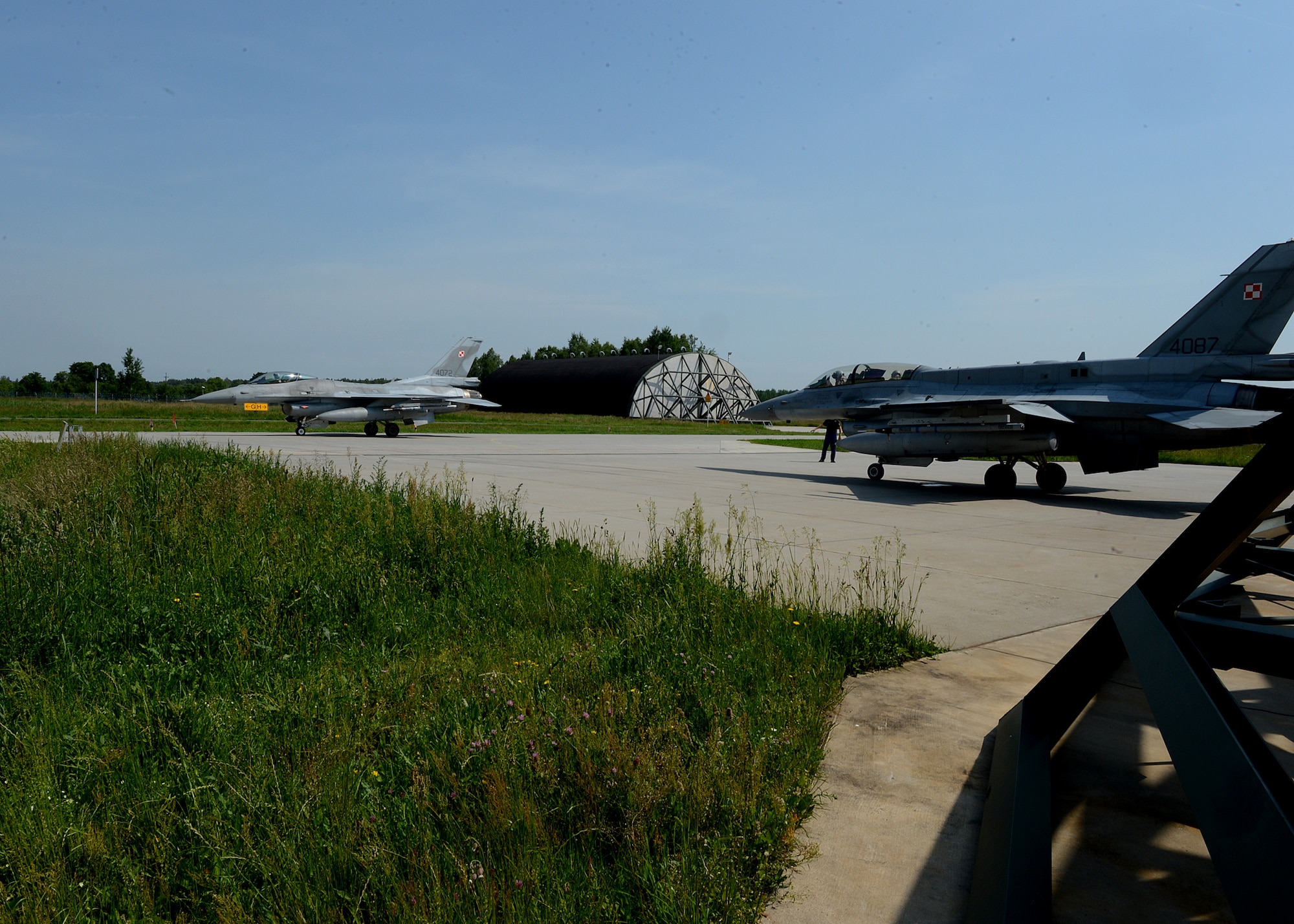 A Polish air force F-16 Fighting Falcon fighter aircraft, left, waits for another aircraft to pass before departure from Lask Air Base, Poland, June 10, 2014. Both aircraft departed to participate in exercise EAGLE TALON with NATO partners. This exercise is similar to exercise RED FLAG that takes place in Nellis Air Force Base, Nev., and Eileson Air Force Base, Ala., which provides aerial combat tactics training in a combined environment. (U.S. Air Force photo by Airman 1st Class Kyle Gese/Released)