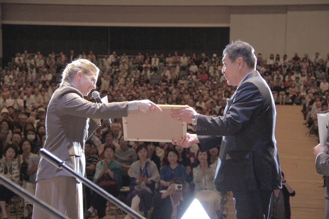 MURAKAMI CITY, Japan -- Capt. Haley Armstrong, Band of the Pacific-Asia commander, presents a keepsake framed photo of the band to Mr. Kazuhiko Hara, Chairman of Nagaoka’s Public Interest Foundation International Exchange Association, during a concert at the Niigata Grand Hotel Concert Hall, Murakami City, Niigata, Japan, June 6, 2014. The performance was part of an eight-day Pacific Showcase concert tour through the Kanetsu area of Japan’s Niigata Prefecture. (U.S. Air Force photo by Staff Sgt. Geoffrey Fisher)