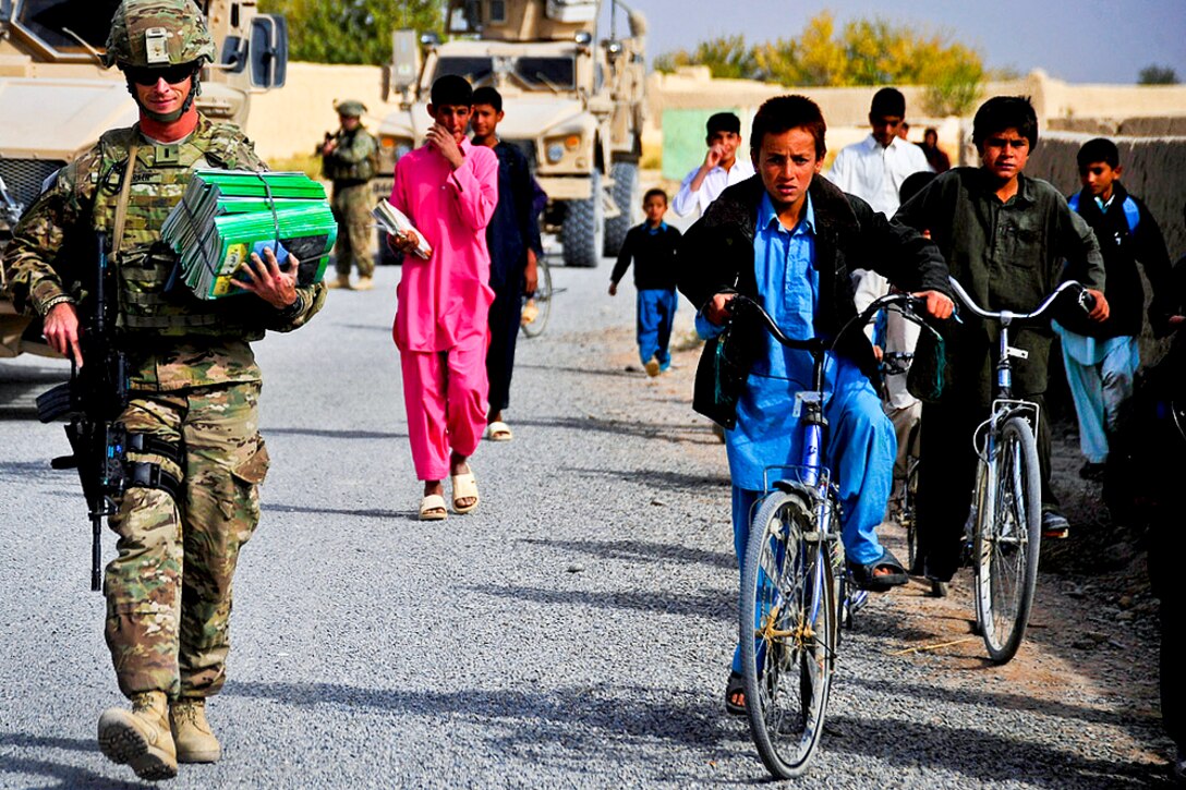 U.S. Navy Lt. j.g. Will Parker, a member of Provincial Reconstruction Team Farah, hands out Sada-e Azadi magazines while other members check on the quality of Nawbahar Road, in the Khak-e Safeyd district in Afghanistan's Farah province, Nov. 16, 2011. The team conducts quality assurance checks on road projects to ensure that contractors meet the construction requirements outlined by the team and government officials.  
