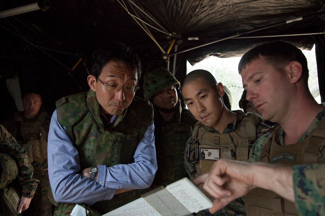 Yoshitoshi Nakamura, center left, follows along as U.S. Marine Staff Sgt. Daniel W. Barron, far right, discusses a graphic firing table while U.S. Marine Gunnery Sgt. Teruhisa Okuyama, center right, translates June 5 at the Ojojihara Maneuver Area, Japan. Nakamura visited the Marines with 3rd Battalion, 12th Marine Regiment, during Artillery Relocation Training Program 14-1 to get a better understanding of how artillery units operate in a field environment. During his visit, Nakamura observed an artillery fire mission and how the unit deploys crew-served weapons to defend their position. Nakamura is the director general of the Tohoku Defense Bureau, Ministry of Defense. Barron is a field artillery operations man with Company C, 1st Battalion, 10th Marines, currently assigned to 12th Marines, 3rd Marine Division, III Marine Expeditionary Force, under the unit deployment program. Okuyama is an intelligence specialist with Marine Aircraft Group 36, 1st Marine Aircraft Wing, III MEF. (U.S. Marine Corps photo by Sgt. Jose O. Nava/Released)