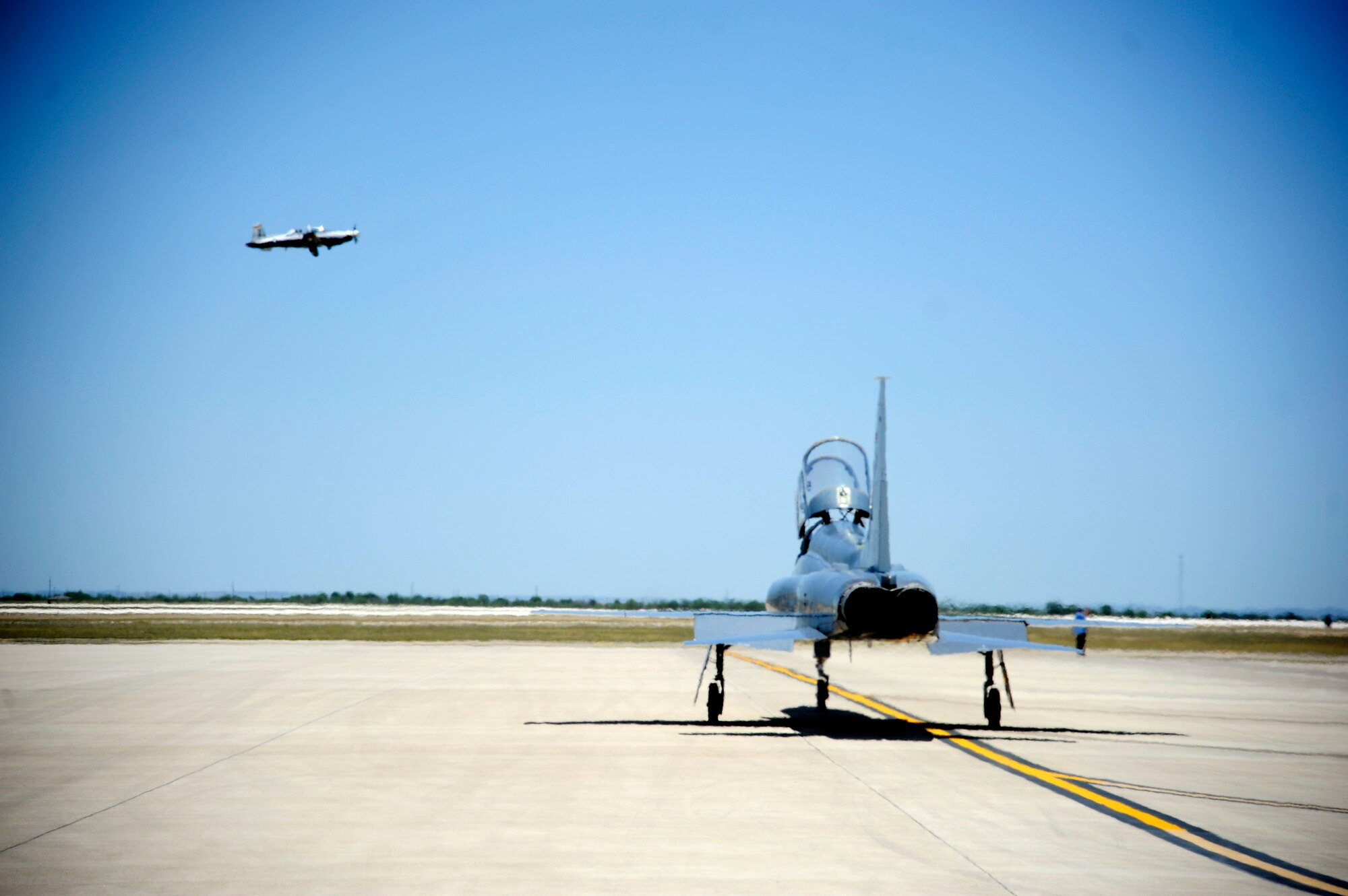 An AT-38B Talon, based out of the 96th Test Group, Holloman Air Force Base, New Mexico, taxi’s to the runway as a T-6 Texan II takes off at Laughlin Air Force Base, Texas, June 10, 2014.  The 47th Flying Training Wing, located at Laughlin Air Force Base, Texas, conducts specialized undergraduate pilot training for the United States Air Force, Air Force Reserve, Air National Guard and allied nation air forces utilizing the T-6, T-38 and T-1A aircraft while deploying mission-ready Airmen, as well as, developing professional, disciplined and bold leaders. (U.S. Air Force photo by Staff Sgt. Steven R. Doty, 47th Flying Training Wing.)(Released)