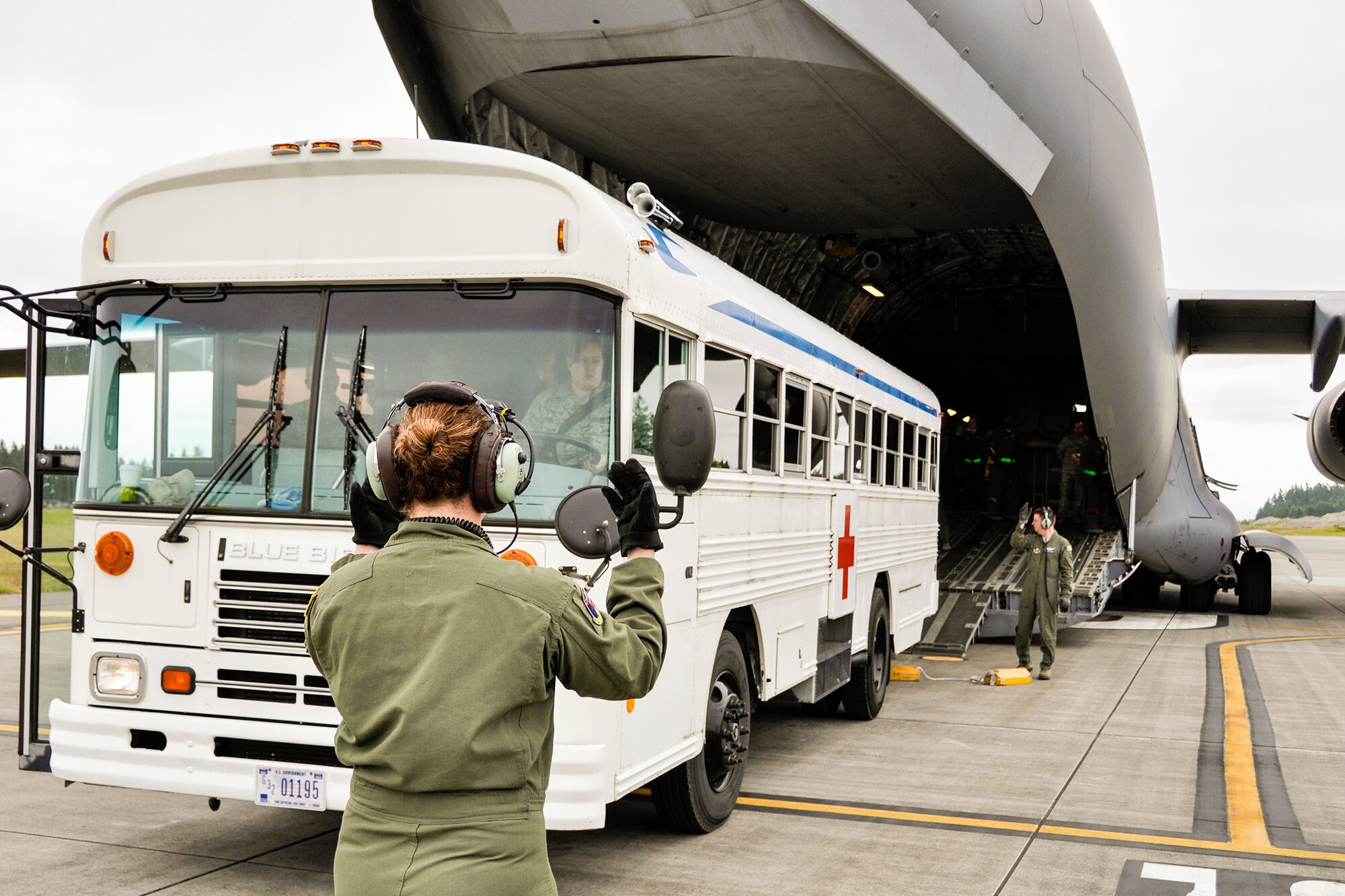 A loadmaster with the 97th Airlift Squadron guides a 446th Aeromedical Staging Squadron bus driver to line up with the ramp of a C-17 Globemaster III aircraft in order to load patients for inflight medical treatment during the Rainer Medic course June 3 at Joint Base Lewis-McChord, Washington. (U.S. Air Force Reserve photo by Jake Chappelle)