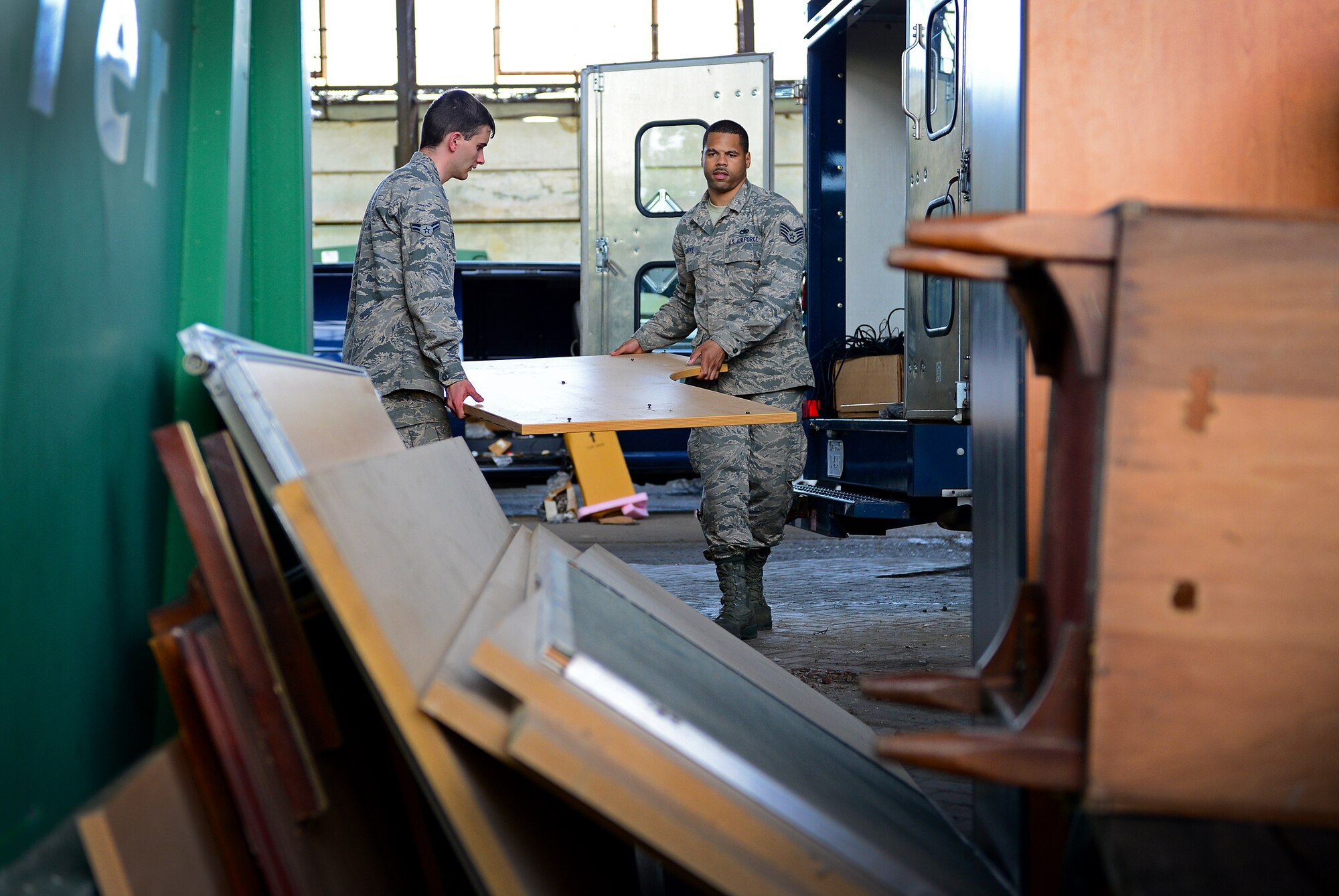 (From left) Airman 1st Class Adam Peeler and Staff Sgt. Aaron Cuffee, 31st Maintenance Squadron, carry office furniture during a base-wide spring cleaning event, May 30, 2014, at Aviano Air Base, Italy. More than 100 Team Aviano vehicles were loaded with government property and unwanted office supplies and discarded into 17 large green containers labeled for items such as batteries, computers, monitors, cords, any metal or plastic, toner cartridges and wood. (U.S. Air Force photo/Senior Airman Matthew Lotz)