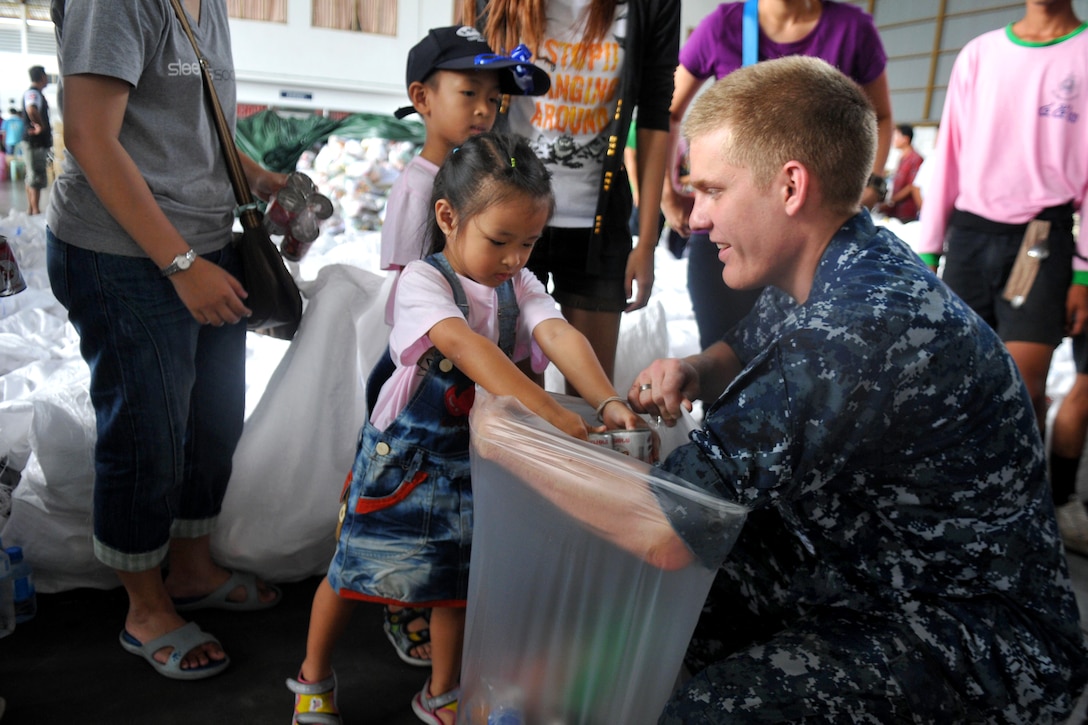 U.S. Navy Petty Officer 2nd Class Leonard Stevenson, assigned to the USS Mustin, receives help from children to prepare packaged goods kits during a community service event in Utapao, Thailand, Oct. 23, 2011. More than 40 sailors from Mustin partnered with members of the Royal Thai Armed Forces in preparing more than 5,000 packages.  
