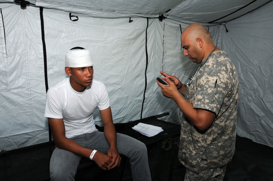 After treating a hurricane victim for a head injury,U. S. Army Sgt. Manuel Olivarez, MEDEL emergency medical technician, enters the patient's treatment information into the Global MedAid program.  In preparation for the 2014 hurricane season, the Joint Task Force-Bravo Medical Element (MEDEL) conducted a humanitarian assistance/disaster response (HA/DR) exercise at Soto Cano Air Base, Honduras June 12, 2014.  The MEDEL's mission was to establish a forward medical treatment operation capable of providing triage, primary care, surgical capabilities, patient holding and evacuation.  As part of this exercise, a suite of mobile technology applications that run on smartphones and tablets were used to enhance the capabilities of the unit: Global MedAid, Medical Application of Speech Translation (MAST) and GeoSHAPE.  (Photo by U. S. Air National Guard Capt. Steven Stubbs)