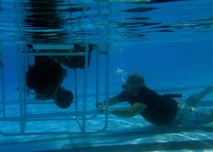 Capt. Josh Hallford, 40th Helicopter Squadron tactics flight commander, prepares to egress from a SWET chair, or shallow water egress trainer, as Corey Ask, Air Force Global Strike Command contracted survival, evasion, resistance and escape program analyst, observes. The SWET chair simulated an inverted helicopter crash. (U.S. Air Force photo/Senior Airman Katrina Heikkinen)