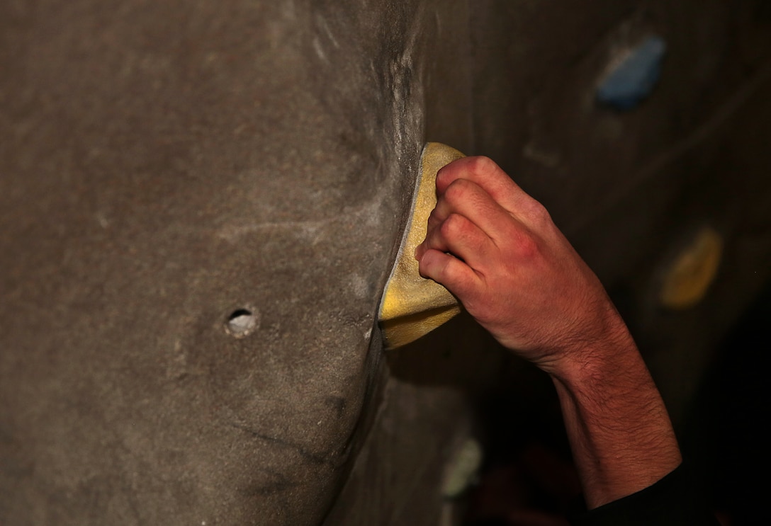 Aric Pope, recreational attendant, West Gym, grips a handle on the rock-climbing wall at the West Gym, June 4, 2014. The wall has several handles located in key positions for participants to place their hands and feet for the climb.

