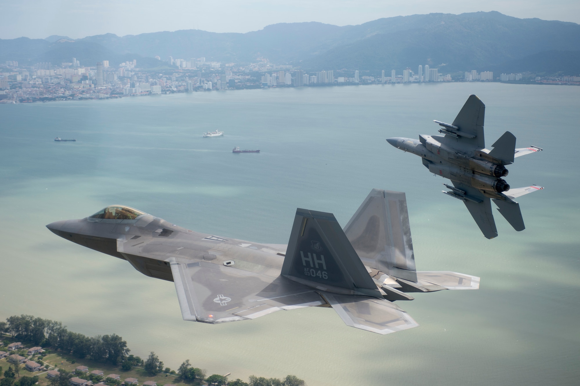 U.S. Air Force F-15 Eagle from the 131st Fighter Squadron, 104th Fighter Wing, Barnes Air National Guard Base, Mass., breaks away from formation with a U.S. Air Force F-22 Raptor from the 154th Wing, Joint Base Pearl Harbor-Hickam, Hawaii, as the two aircraft line up for landing at Royal Malaysian air force P.U. Butterworth, Malaysia, during Cope Taufan 14, June 16, 2014. Cope Taufan is a biennial large force employment exercise taking place June 9 to 20 designed to improve U.S. and Malaysian combined readiness. (U.S. Air Force photo by Tech. Sgt. Jason Robertson/Released) 