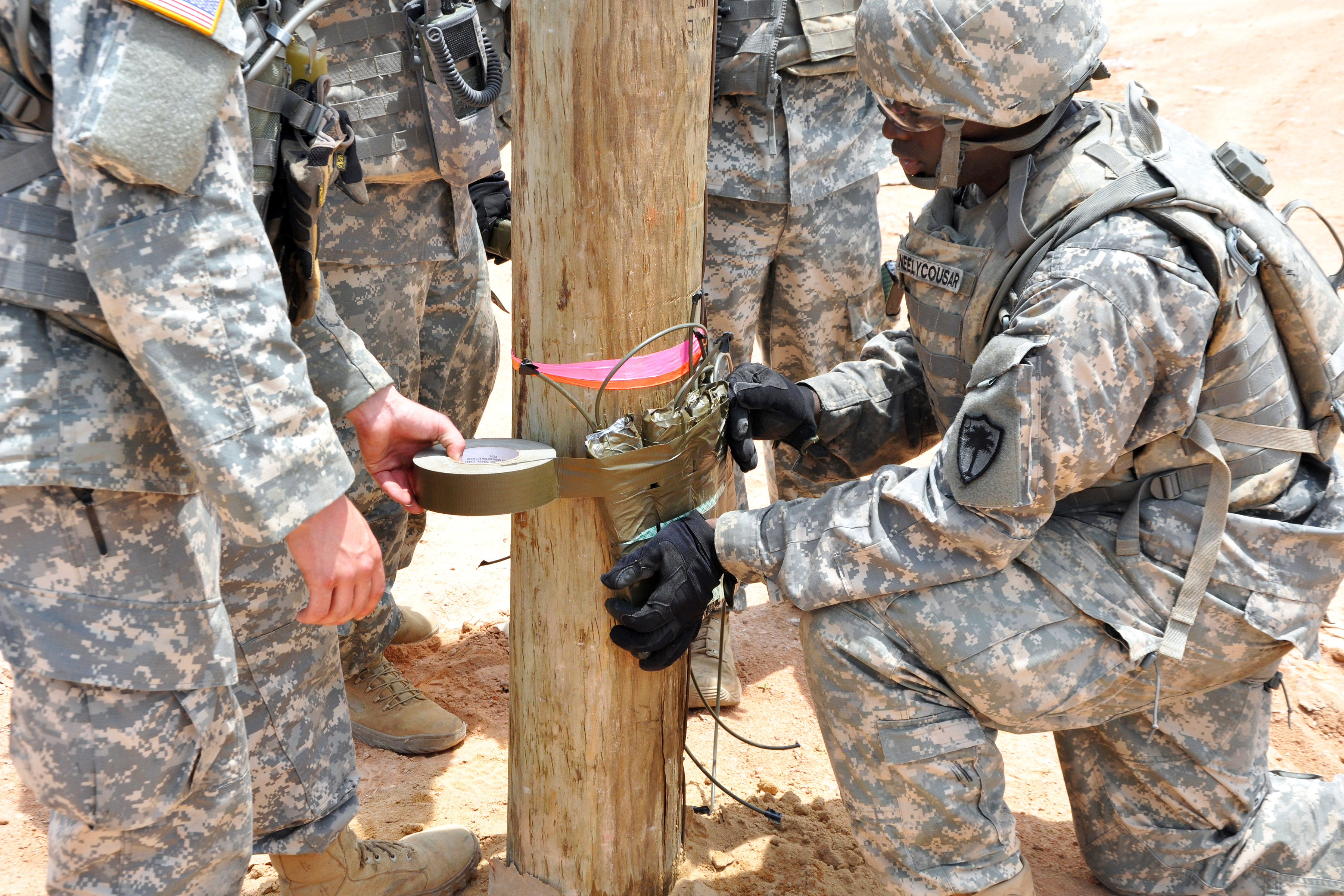 Soldiers use tape to secure a timber cutting charge to a large pole during a demolition range