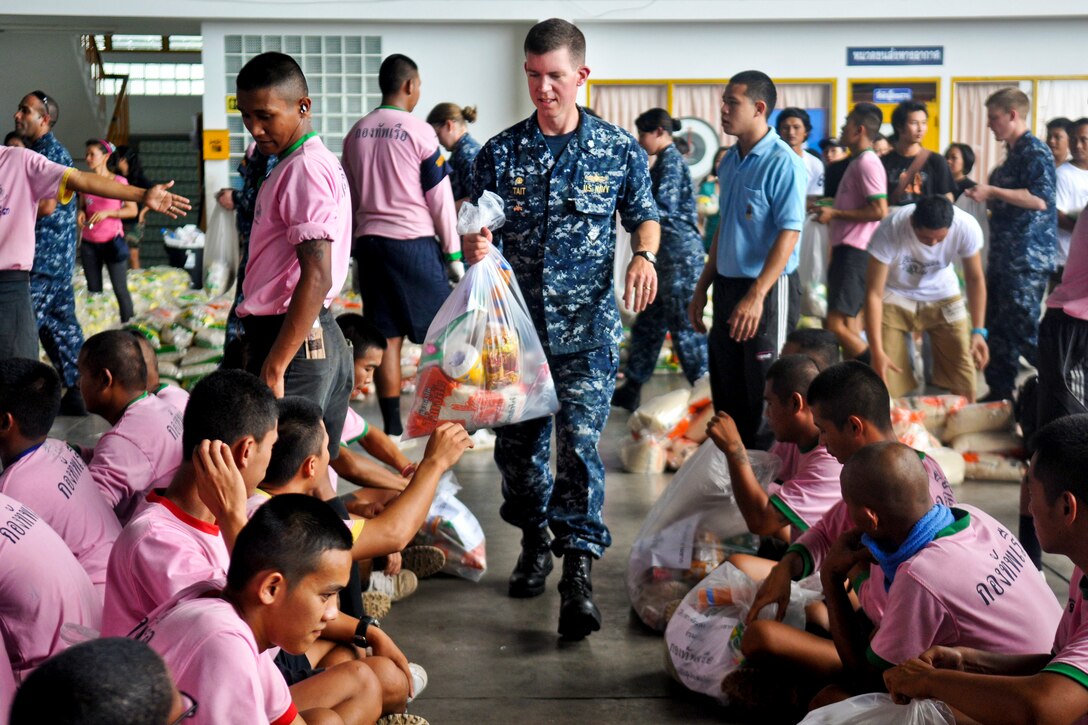 U.S. Navy Cmdr. Scott Tait hands members from the Thai navy a prepared packaged goods kit organized by the Princess Pa Foundation, Thai Red Cross Society, during a community service event, Oct. 23, 2011. Tait is commanding officer of the guided missile destroyer USS Mustin. More than 40 sailors from the Mustin assisted the local community and members of the Thai armed forces with preparing more than 5,000 packages.  
