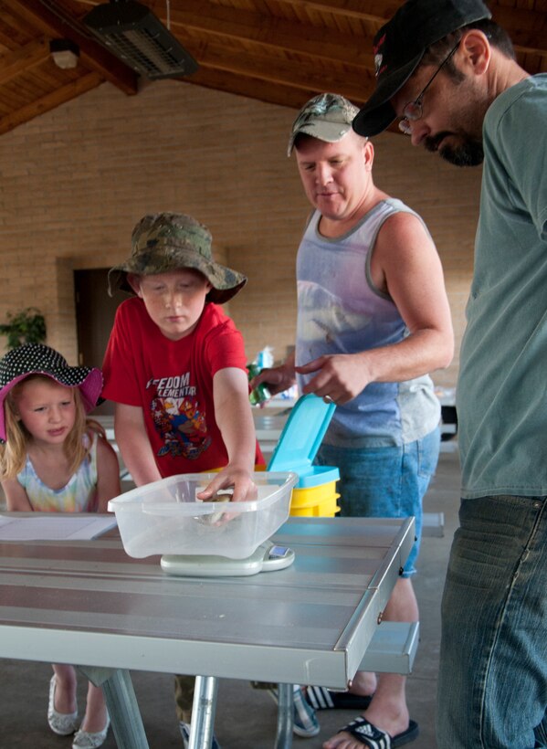 Wyatt, son of Tech. Sgt. Kevin Adams, 90th Missile Security Forces Squadron, (middle-right) places a fish he caught at the F.E. Warren Base Lake during the Father's Day Fishing Derby June 15, 2014, in a scale to be weighed and recorded by Gus Schliffke, 90th Force Support Squadron Outdoor Recreation, for the competitive portion of the fishing derby. (U.S. Air Force photo by Airman 1st Class Jason Wiese)
