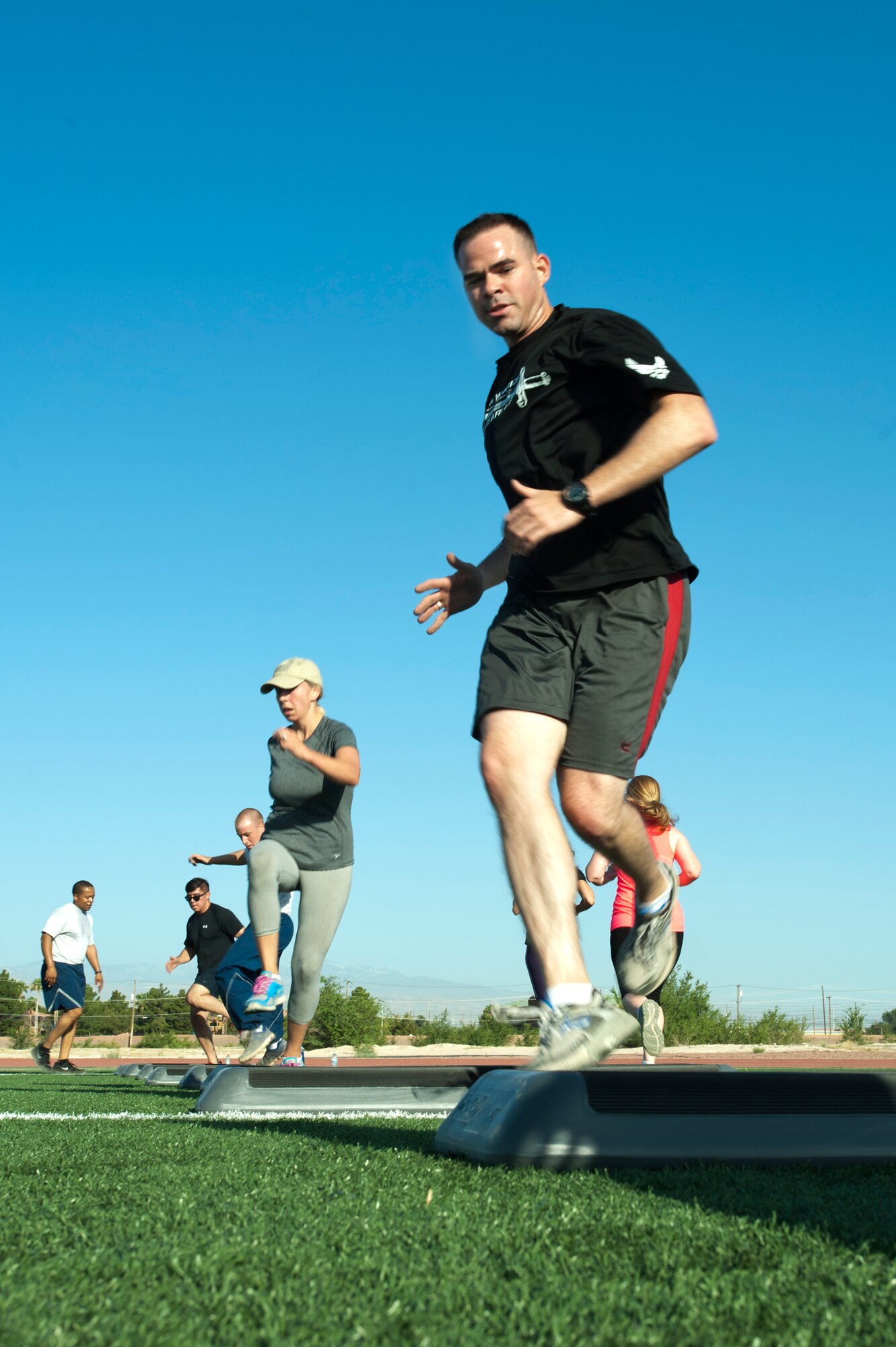 Participants maneuver over aerobic steps as part of the Warrior Trained Fitness exercise session at the Warrior Fitness Center June 12, 2014, at Nellis Air Force Base, Nev. Continuous movement between exercises builds up cardiovascular strength and endurance. (U.S. Air Force photo by Senior Airman Timothy Young)