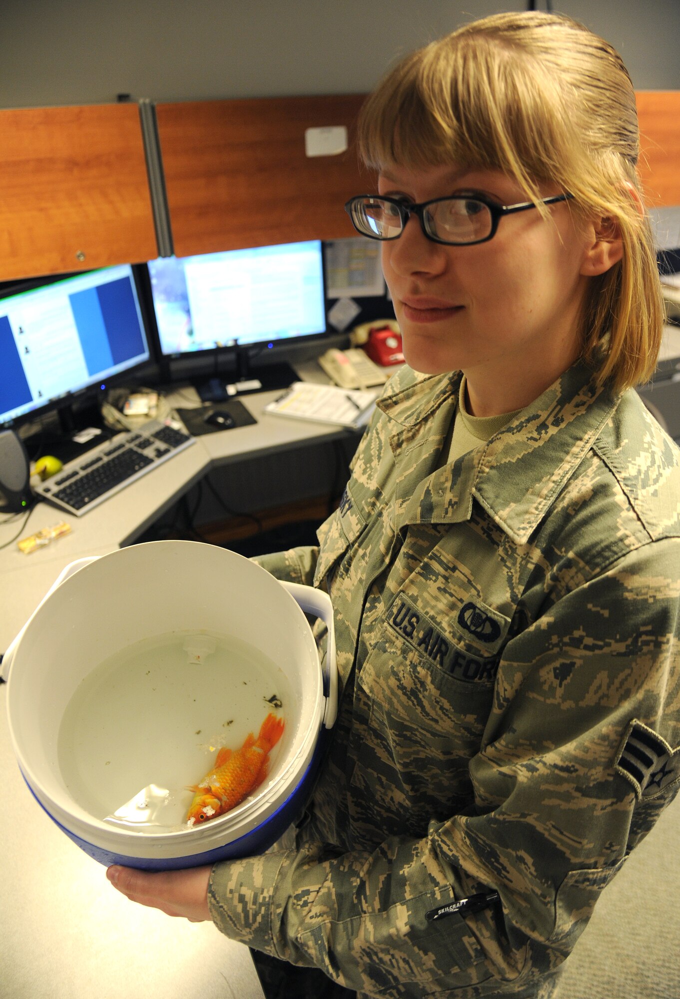 Senior Airman Mary Olesky poses for a photo with a Koi fish she found on the flightline at Fairchild Air Force Base, Wash., June 17, 2014. Olesky spotted the fish while performing a daily airfield inspection. Olesky is the 92nd Operations Support Squadron airfield manager shift lead. (U.S. Air Force photo by Airman 1st Class Janelle Patiño/Released)