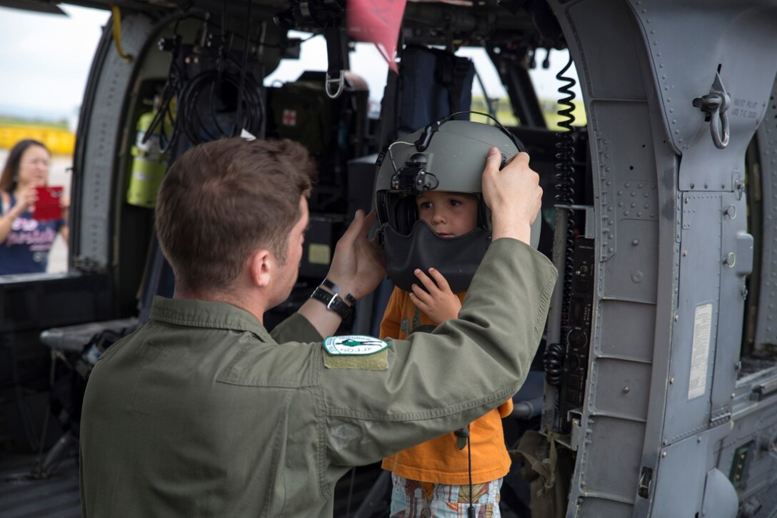 Senior Airman Michael Schlemmer, left, places a HH-60G Pavehawk flight crew helmet on 4-year-old Byron Taylor during the Futenma Flightline Fair June 7 at Marine Corps Air Station Futenma. The fair was an opportunity for community members and service members stationed on Okinawa to get together and learn about the aircraft which is used at MCAS Futenma. Schlemmer is a New Milford, Connecticut, native and special mission aviator with 33rd Rescue Squadron, 18th Wing.(U. S. Marine Corps photo by Lance Cpl. Joey S. Holeman Jr/Released)