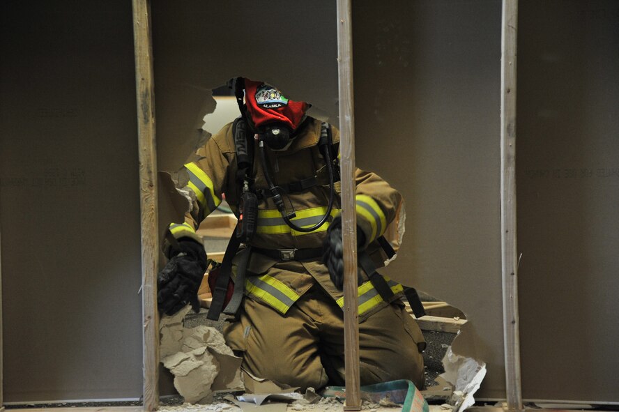 Airmen from Vandenburg Air Force Base, California, break through a simulated wall to find a trapped firefighter while blindfolded during Rapid Intervention Team training at Fairchild Air Force Base, Washington, June 13, 2014. Fairchild hosted 14 Airmen from seven separate fire stations throughout the Air Force Space Command. Teams of two train together in buildings compiled with scenarios that help mimic the real life possibilities of being trapped, injured or lost. (U.S. Air Force photo/Staff Sgt. Alexandre Montes)
