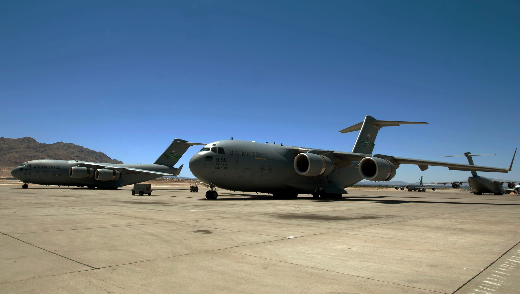 Two C-17 Globemasters assigned to the 62nd Airlift Wing, McChord Air Force Base, Wash. park on the Nellis AFB flightline June 17, 2014.  The C-17s are temporally deployed to Nellis in support of the U.S. Air Forces Weapons School, Joint Forcible Entry.  JFE is part of the school’s Advanced integration phase.  (U.S. Air Force photo by Airman 1st Class Rachel Loftis)   