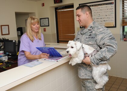 Donna Bothe, Joint Base San Antonio-Randolph Veterinary Clinic office manager, assists Lt. Col. Erwin Larios, Air Force Space Command 318th Operations Support Squadron director of operations, and his dog, Max, during a routine visit June 5 at the JBSA-Randolph Veterinary Clinic. All dogs and cats that live on base are required to be vaccinated for rabies in accordance with state laws. (U.S. Air Force photo by Melissa Peterson)