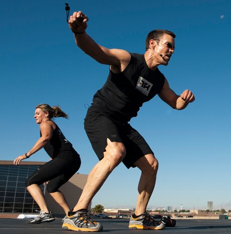 Missy Cornish (left), wife of Col. Barry Cornish, 99th Air Base Wing commander and Tony Horton, P90X workout creator, perform a series of jumping exercises while leading a Warrior Trained Fitness session at the Warrior Fitness Center, June 17, 2014, at Nellis Air Force Base, Nev. The various exercises were meant to increase muscular and cardiovascular strength. (U.S. Air Force photo by Airman 1st Class Thomas Spangler)