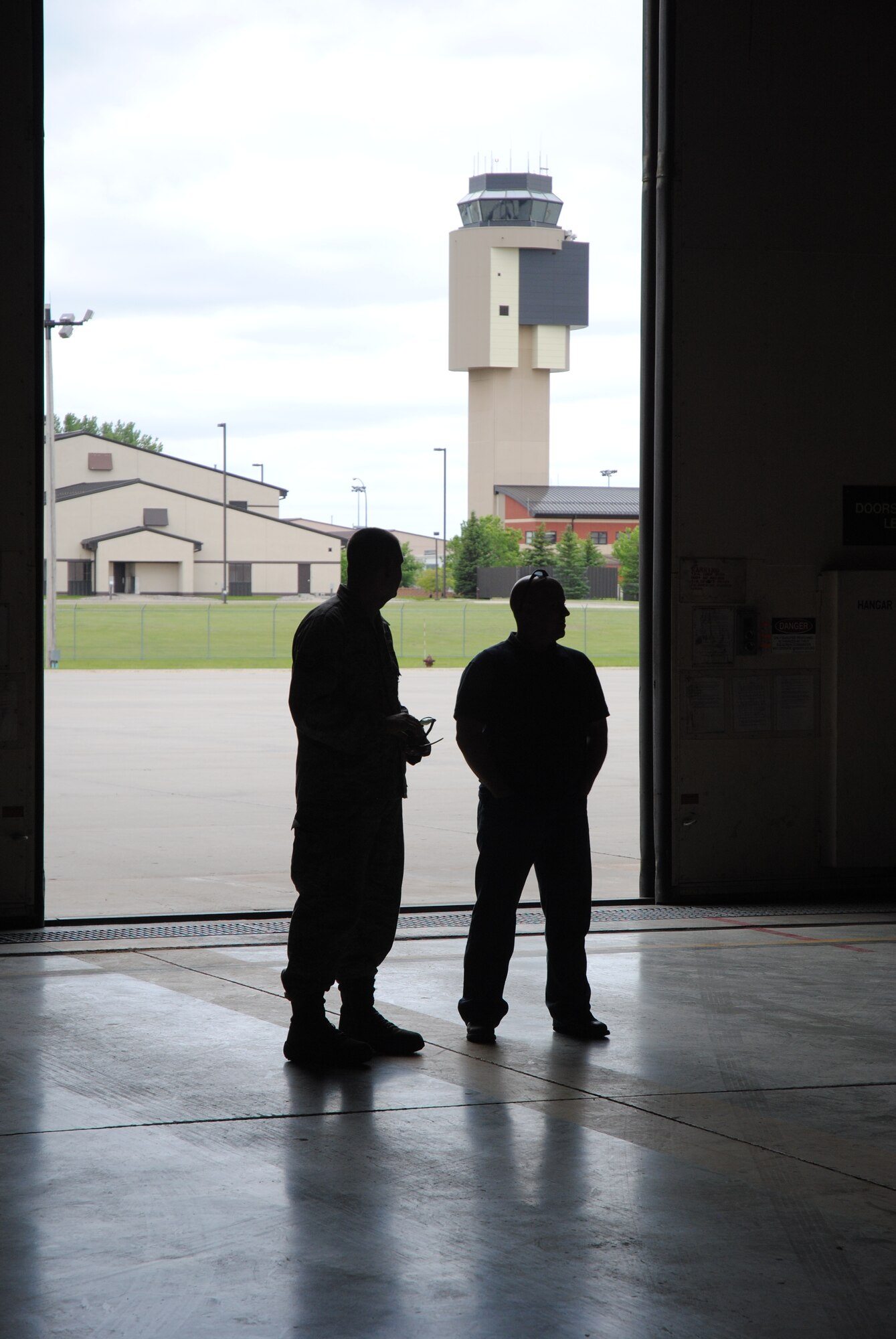 With the air traffic control tower in the background, Tech. Sgt. Clinton Hammons and Andrew Swenson from the 319th Air Base Wing Safety Office cast shadow as they watch more than 50 people tour one of the hangars that house some of the unmanned aircraft vehicle operated by a tenant unit on Grand Forks Air Force Base, N.D. The viewing of the UAVs was one of the highlights in the tour provided for guests attending the 2014 M.A.C.A. Civil Fly-In, which took place June 14, 2014. (U.S. Air Force photo/Staff Sgt. Luis Loza Gutierrez)