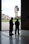 With the air traffic control tower in the background, Tech. Sgt. Clinton Hammons and Andrew Swenson from the 319th Air Base Wing Safety Office cast shadow as they watch more than 50 people tour one of the hangars that house some of the unmanned aircraft vehicle operated by a tenant unit on Grand Forks Air Force Base, N.D. The viewing of the UAVs was one of the highlights in the tour provided for guests attending the 2014 M.A.C.A. Civil Fly-In, which took place June 14, 2014. (U.S. Air Force photo/Staff Sgt. Luis Loza Gutierrez)