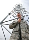 With a hand-held microphone in his grips, Airman Anthony Kelly, a 319th Communications Squadron high-frequency global communication system operator, poses in front of a radio tower on Grand Forks Air Force Base, N.D., June 16, 2014. Kelly a native of Worcester, Mass., was named Warrior of the Week for the third week of June 2014. (U.S. Air Force photo/Senior Airman Xavier Navarro)
