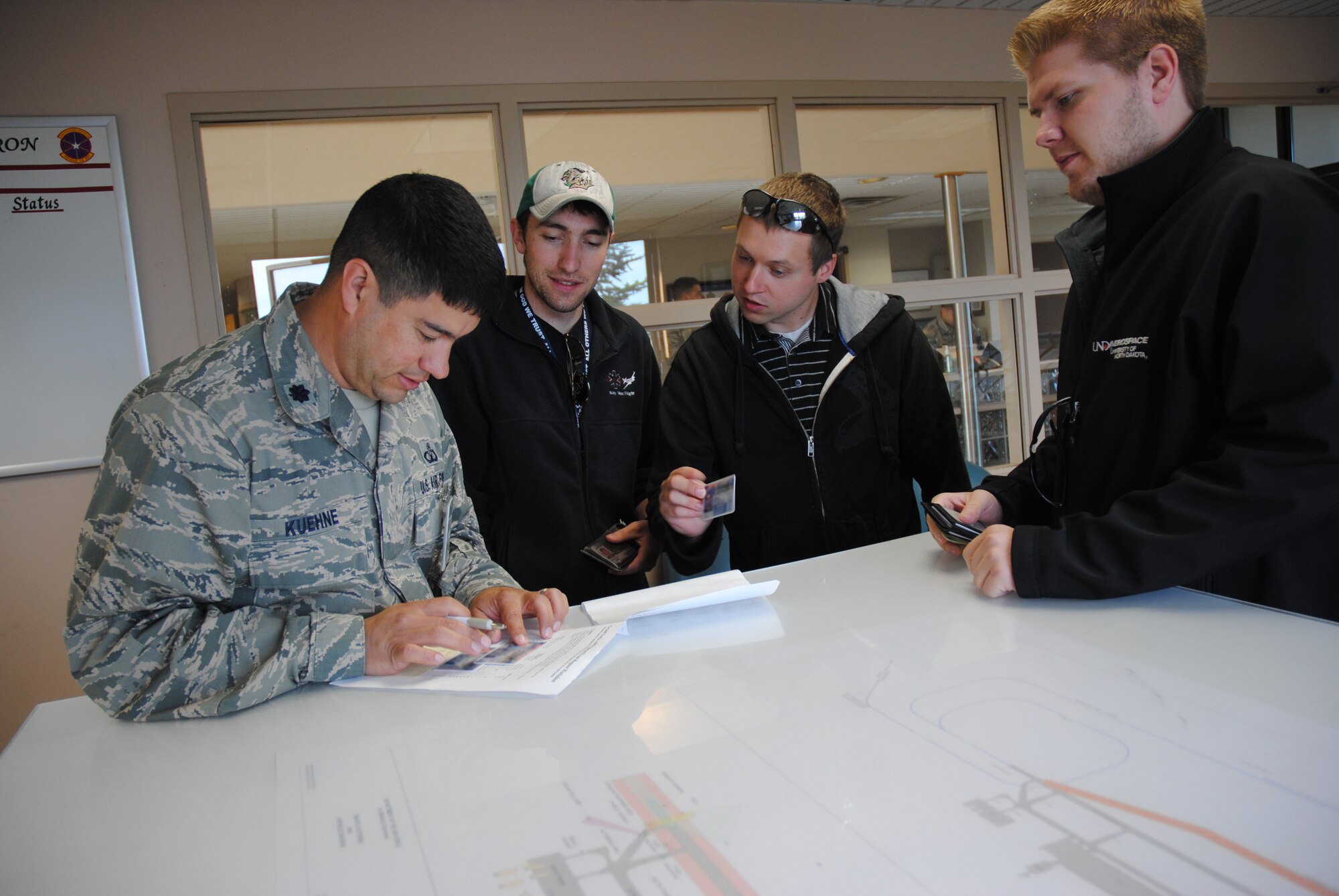 Using a checklist of approved guests, Lt. Col. Rudolf Kuehne, 319th Air Base Wing chief of safety, verifies the identity of three men attending the 2014 M.A.C.A. Civil Fly-In held June 14, 2014, on Grand Forks Air Force Base, N.D. The trio was on several pilots who were temporarily granted permission to land on the installation in order to attend the event, which is centered around the safety office's Mid-Air Collision Avoidance program. (U.S. Air Force photo/Staff Sgt. Luis Loza Gutierrez)