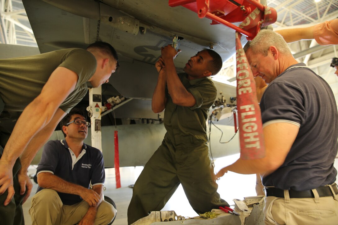 Boeing field service representatives answer questions and assist Marines with maintenance on the wing of an AV-8B Harrier inside the Marine Attack Squadron 542 hangar. Boeing FSRs act as mentors to Marines in areas like avionics, airframes, power line, crew safety systems and supply.