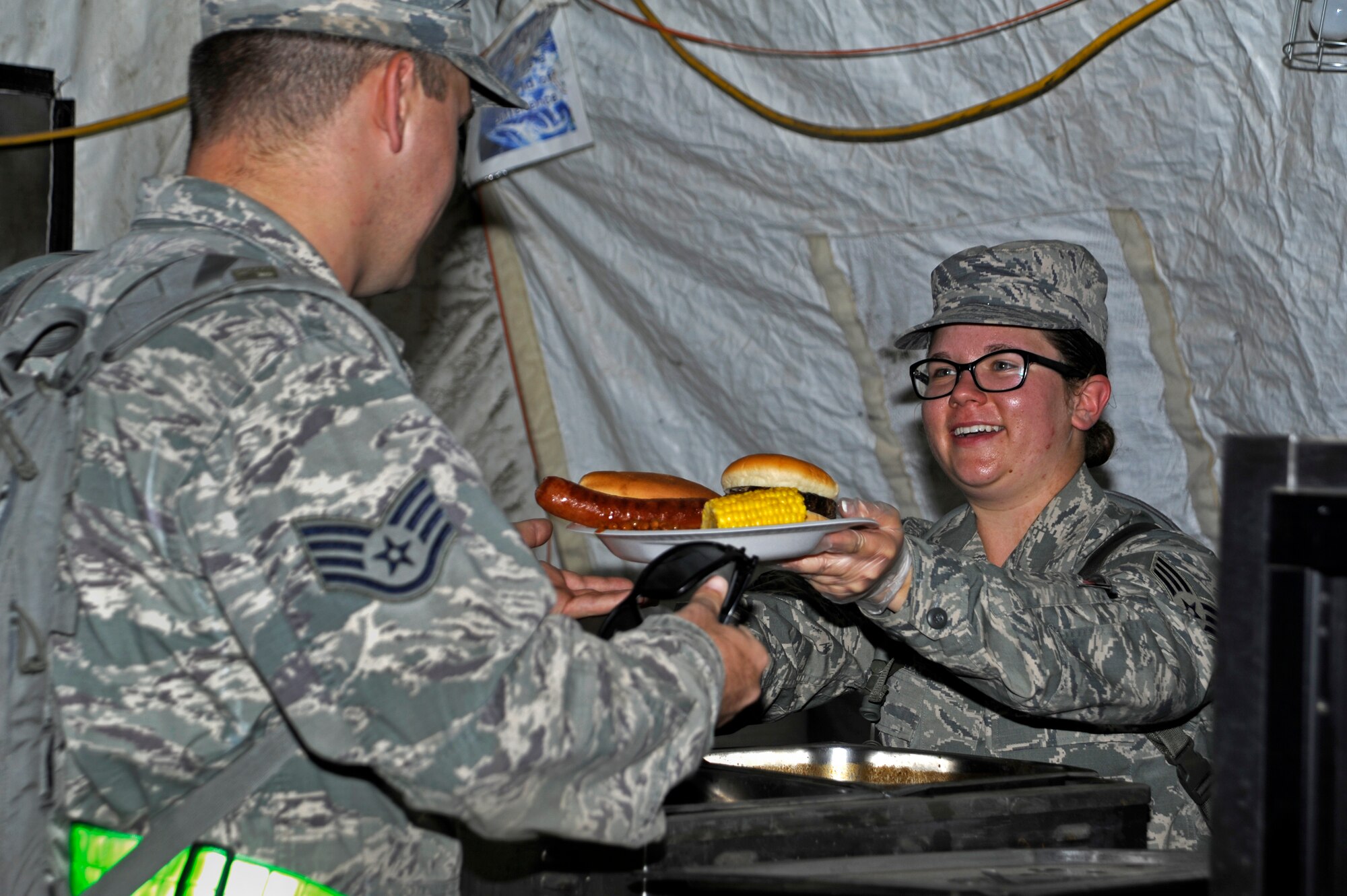 U.S. Air Force Senior Airman Brenna Grupe, 355th Force Support Squadron food service accountant, hands an Airman a plate of hot food at a deployed dining facility at “Base X” during an Operational Readiness Exercise at Davis-Monthan Air Force Base, Ariz., June 17, 2014. During exercises, Airmen are placed in a simulated deployed location and tested on how they perform their duties during random base attacks. (U.S. Air Force photo by Airman 1st Class Betty R. Chevalier/Released)