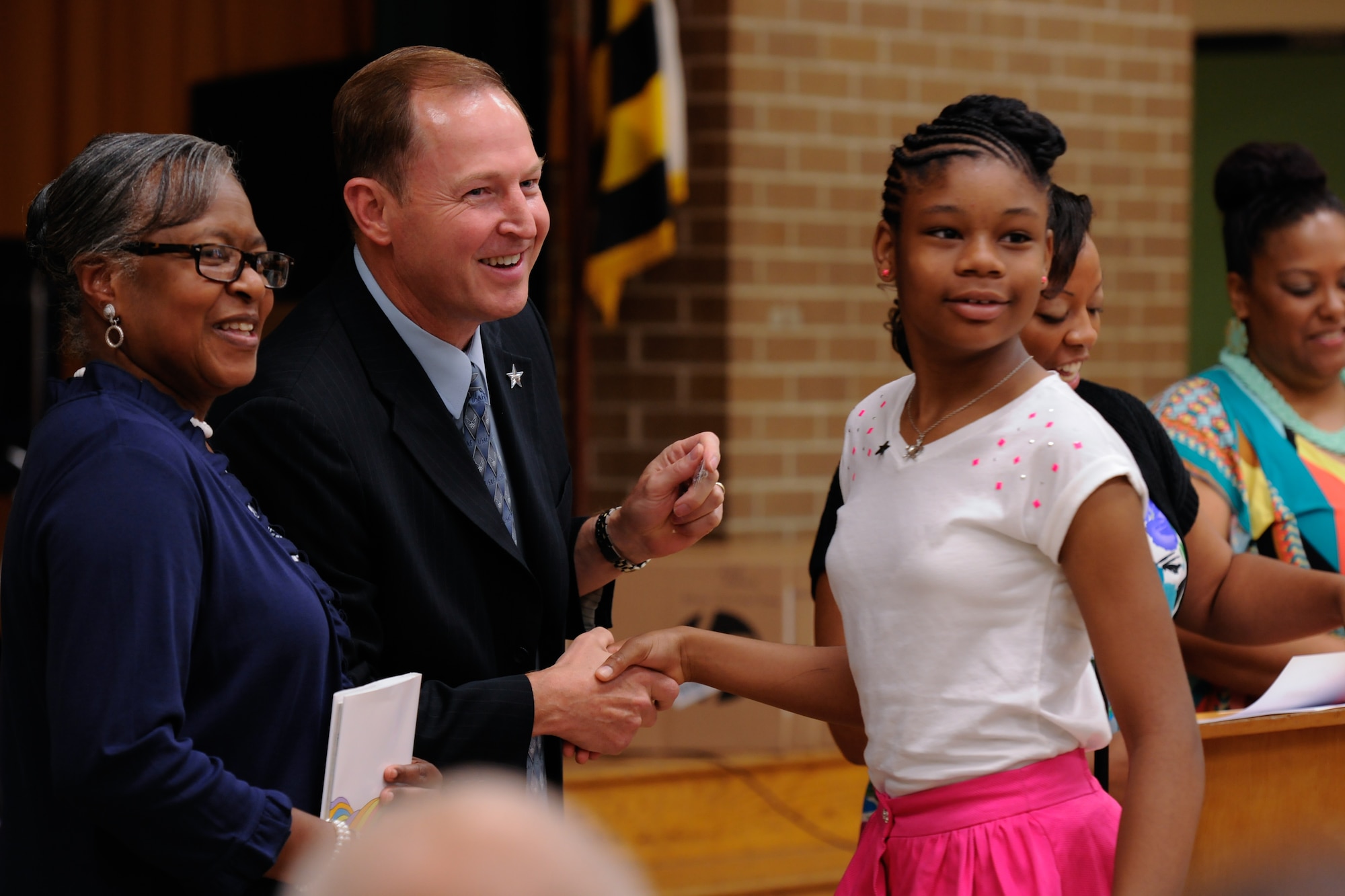 Anaya Jackson turns to look at her cheering mother, Tamika Gaskins, as she receives a silver star pin from John Rogers, Joint Base Andrews 844th Communications Group deputy director, at the Francis T. Evans Elementary School fifth grade graduation ceremony, Clinton, Md., June 12. The 844th CG adopted and has sponsored the school for the past three years. The students completed an eight-month mentorship program with Joint Base Andrews Airmen coordinated through the Area Coalitions Education-Excellence program that connects public schools with government, military, private sector and local community volunteers. (U.S. Air Force photo/Aimee Fujikawa)