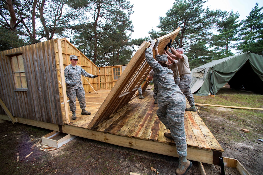 U.S. airmen and the British army's 39 Engineer Regiment raise the front wall on single room structure that was dissembled so it could be moved to a more suitable site during Exercise Flying Rose at Kinloss Barracks in Forres, Moray, Scotland, June 13, 2014.