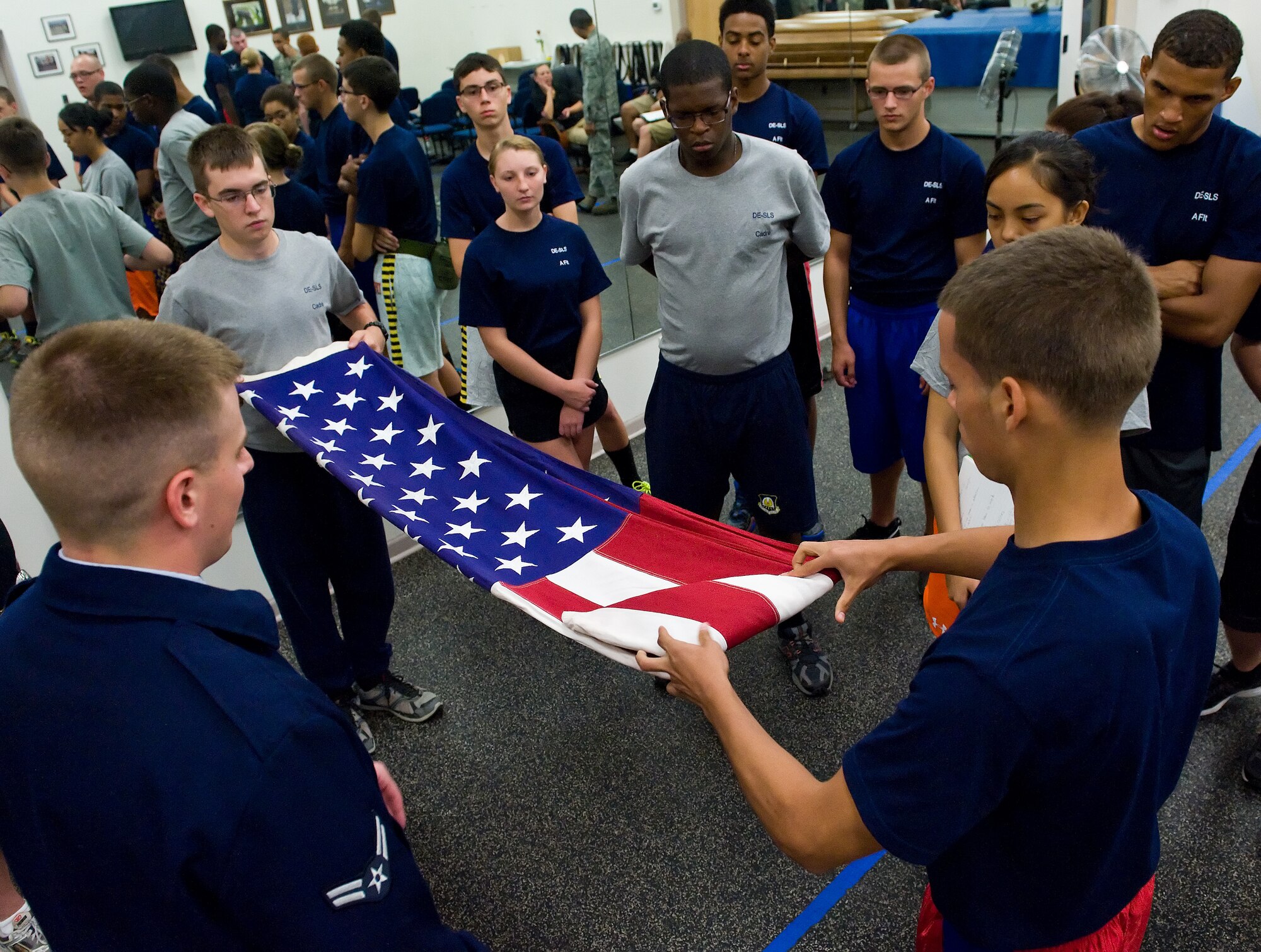 Airman 1st Class Jacob Lassiter, bottom left, Dover Air Force Base Honor Guard member, watches Air Force junior ROTC cadets Russell Stanley, upper left, Smyrna High School, Smyrna, Del. and Tyler Bucanan, right, William Penn High School, New Castle, Del., fold the U.S. flag June 18, 2014, at Dover Air Force Base, Del. Lassiter and other Dover AFB honor guard members provided cadets with hands-on training on honor guard duties and tasks. (U.S. Air Force photo/Roland Balik)