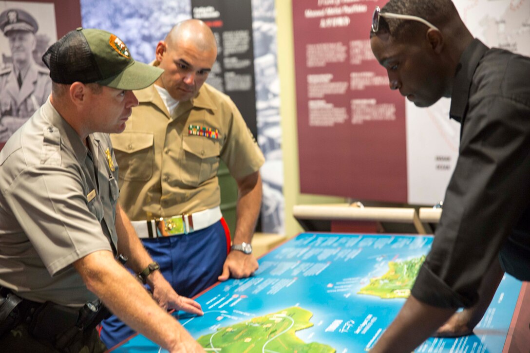 Jayson B. Tinney, left, shows Gunnery Sgt. Francisco M. Gaxiola, center, and Sgt. Andre M. Thomas a map of the battles of Saipan and Tinian June 13 at the American Memorial Park on Saipan. Marine musicians and a color guard detail took part in the 70th Anniversary Reunion of Honor ceremonies at Tinian and Saipan. The ceremonies were held to mark a milestone of peace in the region and to pay tribute to both U.S. and Japan veterans of the battles of Saipan and Tinian during World War II. Tinney is park ranger with the U.S. Park Service and resident of Saipan. Gaxiola is the enlisted conductor with the III Marine Expeditionary Force Band and Los Angeles, California, native. Thomas is an automotive organizational technician with Headquarters Battalion, 3rd Marine Division, III MEF, and Miami, Florida, native. 