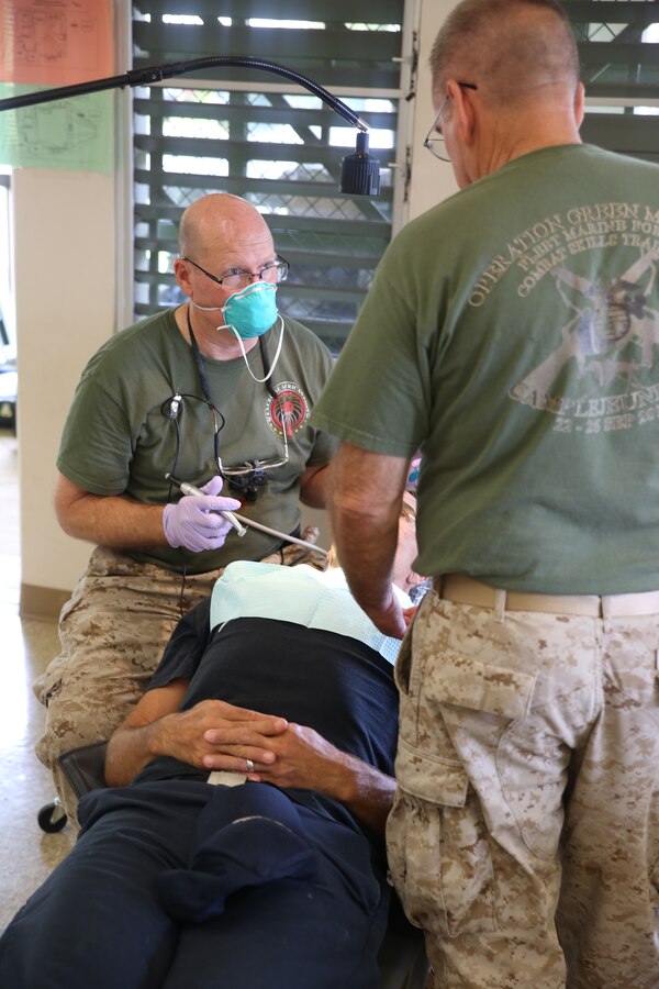Lieutenant Cmdr. Forrest Kroschel (Front) and Lt. Cmdr. Stewart Powers (Back), both dentists with 4th Dental Battalion, 4th Marine Logistics Group, work together to care for a patient at the mobile site June 19, during Innovative Readiness Training exercise Tropic Care 2014, Kauai , Hawaii.  The mobile site is an off -branch of the three main sites that patients can be seen for medical, dental and optometry care provided by the Department of Defense at no cost to the public, providing simultaneous military training for medical personnel. TC14 also allows service members from each branch to combine their expertise in a joint-training environment.   