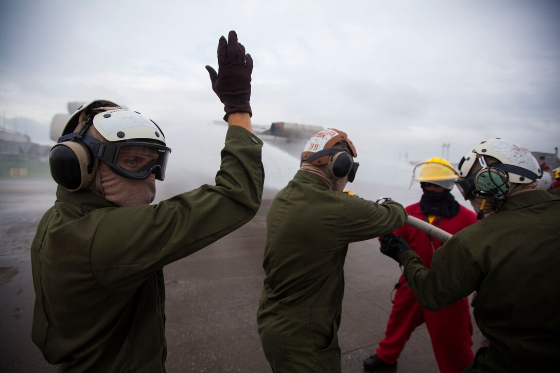 A Marine with Marine Medium Tiltrotor Squadron 262 (Reinforced), 31st Marine Expeditionary Unit, signals his team to rotate from the hose nozzle during a crash fire rescue scenario with the Mobile Aircraft Firefighting Training Device at the base fire station, June 19, 2014. The week-long course instructed Marines on advancing and sweeping techniques with the hoses on a burning mock aircraft. The Marines are not from firefighting billets but are taught to be first-responders to potential aircraft accidents when the unit is embarked aboard Navy ships with the MEU. The 31st MEU is the force of choice for the Asia-Pacific and is the only continuously forward-deployed MEU.