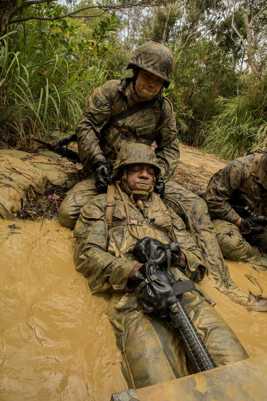 Cpl. James E. King, top, pulls Lance Cpl. Laquan K. Wilkerson out of a water obstacle during the jungle endurance course June 20 at the Jungle Warfare Training Center on Camp Gonsalves, Marine Corps Base Camp Smedley D. Butler, Marine Corps Installations Pacific. During this portion of the course, participants use their weapons to push up concertina wire, low crawl through narrow trenches, and submerge under water while following a length of rope until an instructor pulls them up. King is a New York, New York, native and warehouse clerk, and Wilkerson is a Gaithersburg, Maryland, native and field wireman. Both are with 1st Battalion, 8th Marine Regiment, which is currently assigned to 4th Marines, 3rd Marine Division, III Marine Expeditionary Force, under the unit deployment program. (U.S. Marine Corps photo by Lance Cpl. Diamond N. Peden/Released)

