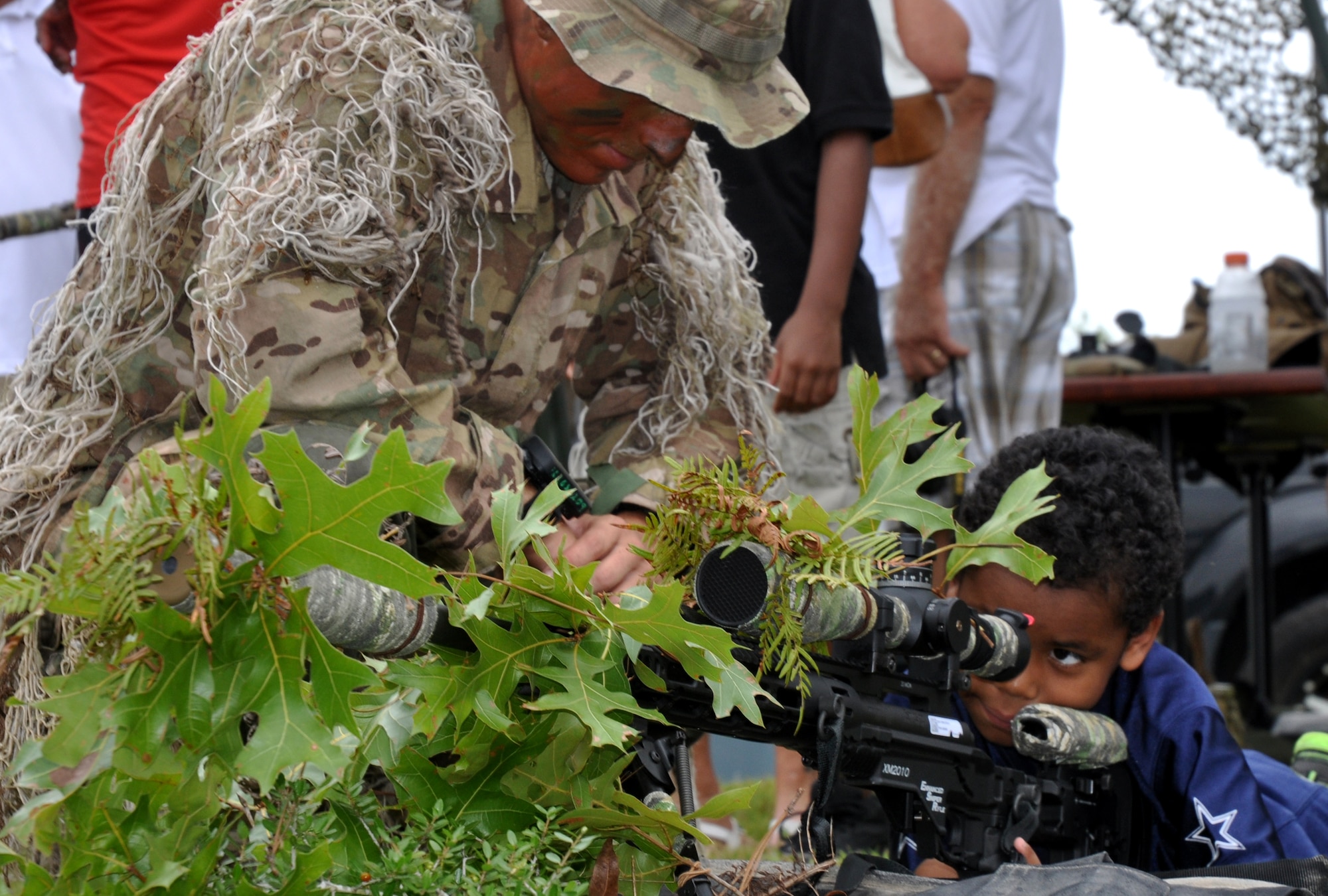 Sgt.1st Class Matt Bius shows a child how he uses the scope of a sniper rifle at the 7th Special Forces Group (Airborne) annual open house June 24 at their headquarters on Eglin's range. The 7th SFG (A) invited members of the Northwest Florida community onto their Compound for the Red Empire Community Day.  The day's events featured recognition of the Group's distinguished volunteers and a parachute demonstration by the U.S. Special Operations Command Para-Commandos.  After the opening ceremony, attendees visited displays manned by Group soldiers to learn more about the 7th SFG (A), its soldiers and its missions. (U.S. Air Force photo/Chrissy Cuttita)