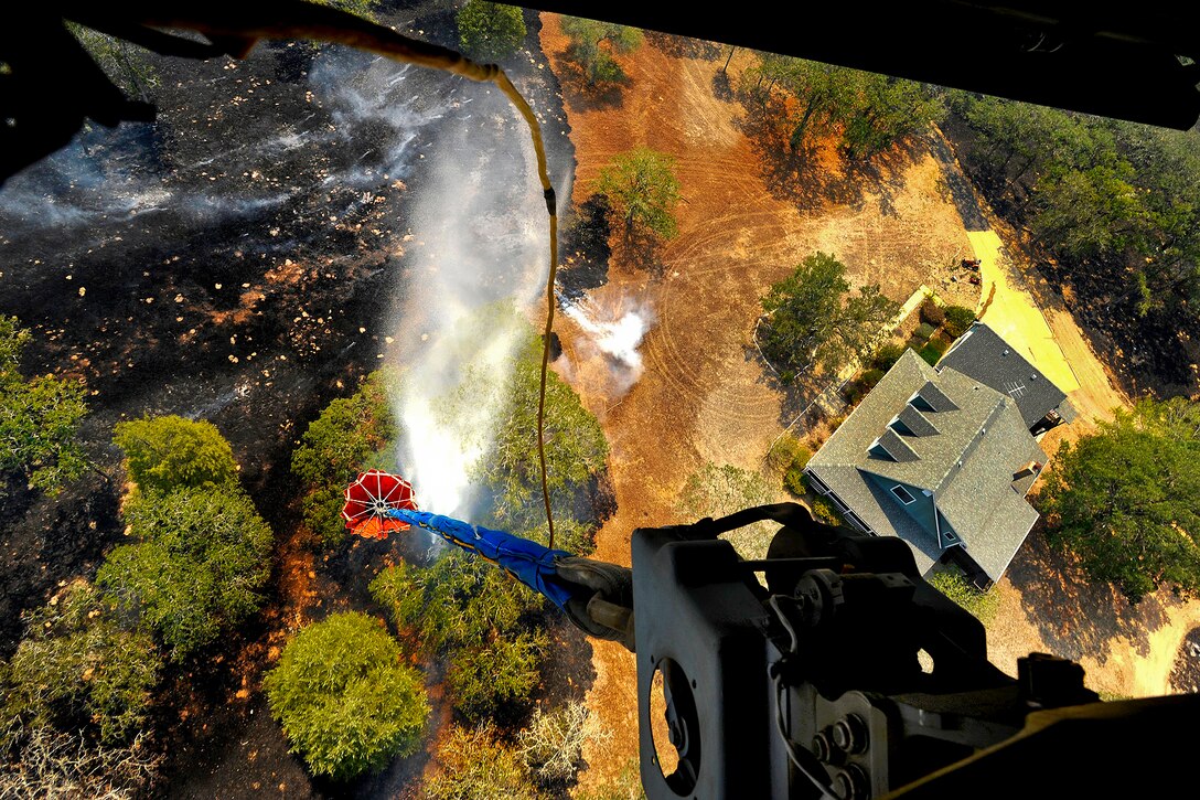 Soldiers aboard a Texas Army National Guard CH-47 Chinook helicopter dump water from a collapsible firefighting bucket onto a wildfire burning at the edge of a residential area near Bastrop, Texas, Sept. 6, 2011.  
