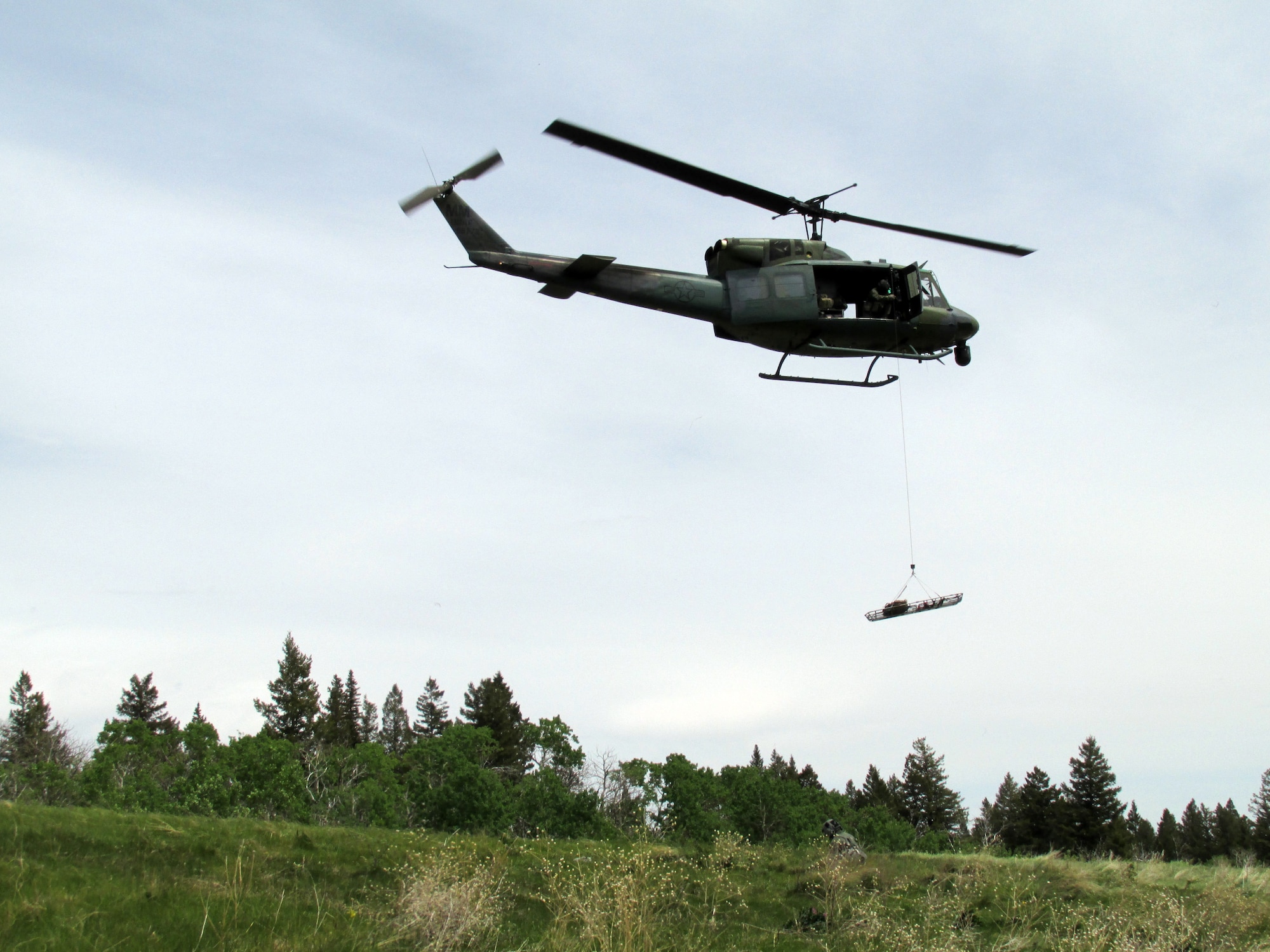 The crew (Blade 99) from the 40th Helicopter Squadron lowers a Stokes litter to Maj. Rhodora Beckinger, 341st Medical Operations Squadron flight surgeon, on the ground. The Stokes litter is a rescue device that allows unconscious or non-ambulatory patients to be hoisted out of remote locations. (Courtesy Photo)