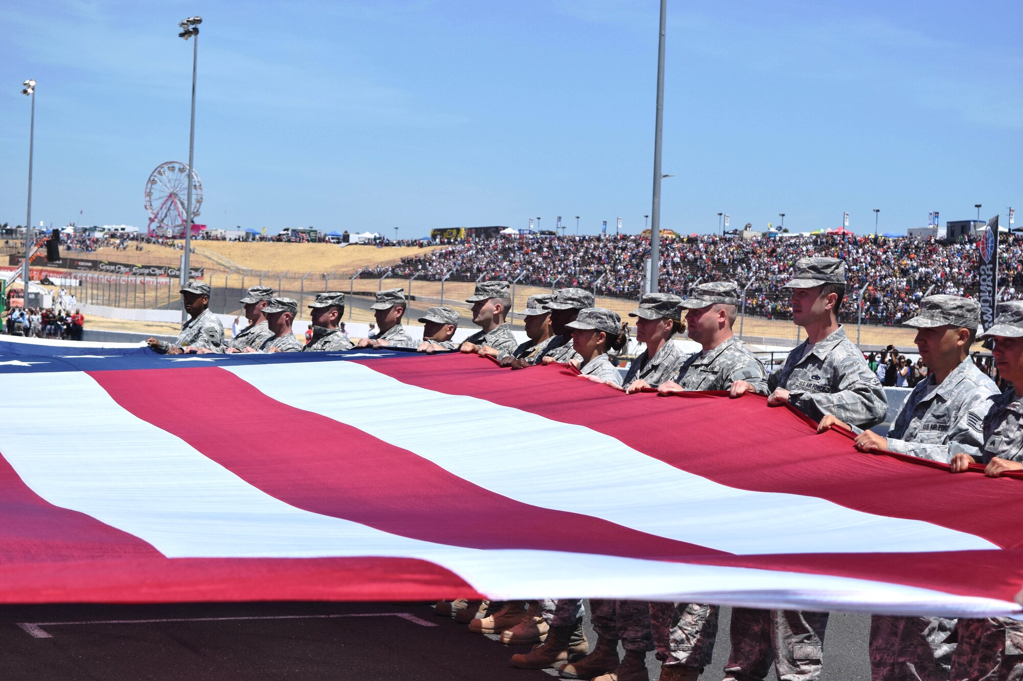 Beale Air Force Base Airmen and Army soldiers hold a large American flag during pre-race ceremonies at the NASCAR race at Sonoma Raceway, Sonoma, Calif., June 22, 2014. Thirty Airmen volunteered to hold the flag during the National Anthem and got to enjoy the race afterwards. (U.S. Air Force photo by Capt. Brian Wagner/Released)