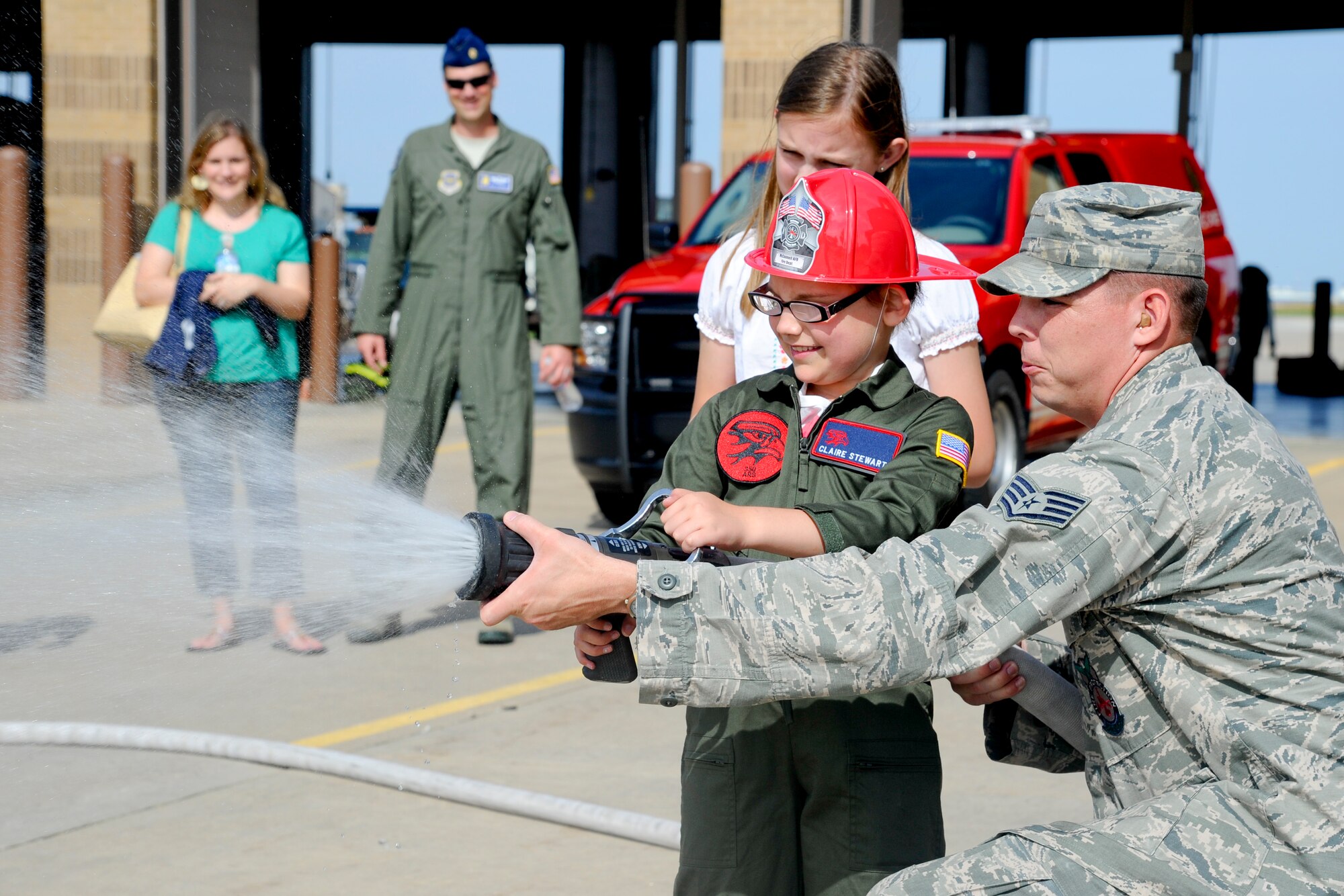 Staff Sgt. Brandon Martin, 22nd Civil Engineer Squadron firefighter crew chief, uses a hose with Claire Stewart, Team McConnell’s “Pilot for a Day,” June 20, 2014, at McConnell Air Force Base, Kan. Several base units gave Stewart a tour through their operational environment and had several activities and demonstrations planned for her to enjoy. (U.S. Air Force photo/Airman 1st Class John Linzmeier)