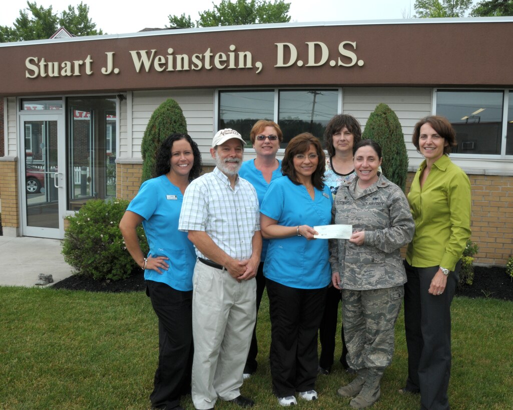 Ms. Mary Grace Scarpelli (center), Operation Whiter-Brighter Coordinator from Advanced Dental presents a check for over $3,700 to Captain Gina Pizziconi Cupples, 914th Logistics Readiness Squadron commander and president of Friends of Family Support XXXXXXX at Advanced Dental in Niagara Falls, N.Y. on June 25, 2014. Looking on are (left to right) Ms. Cindy Garner, dental assistant, Dr. Stuart J. Weinstein, dentist, Ms. Susan Yuroshoski, supervising assistant, Ms. Nancy Mastromatteo, office manager, and Ms. Patty Braun, 914th Airlift Wing executive officer.  Dr. Weinstein and his staff presented a check of proceeds collected from their Operation Whiter-Brighter Campaign. Each year several thousands of dollars are collected to be used for various programs to benefit local military members and their families. (U.S. Air Force photo by Peter Borys)