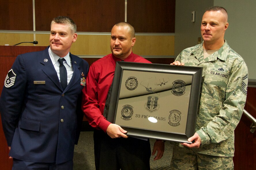 Airmen of the 33rd Fighter Wing present the guest speaker, retired Tech Sgt. Jerry Sasser, with a plaque for his service to the wing during the Khobar Towers memorial ceremony June 25 at Eglin Air Force Base, Fla. Sasser was one of the survivors of the tragic bombing that killed 19 service members, including 12 33rd Fighter Wing Airmen. Each year a ceremony is held by the Nomads to commemorate their brothers who’ve “ceased their wandering.” (U.S. Air Force photo/Sara Vidoni)