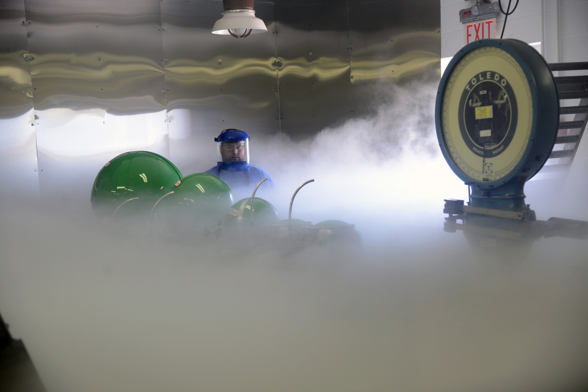 As the room fills with “smoke,” Bradley Lange and Zach McCain make sure converters are being filled with liquid oxygen safely and correctly in the Oxygen Maintenance Depot’s Fill Room. The employees who work in this room have to wear the required safety gear because liquid oxygen’s freezing point is 50.5K, or -368.77 Fahrenheit. (Air Force photos by Kelly White)