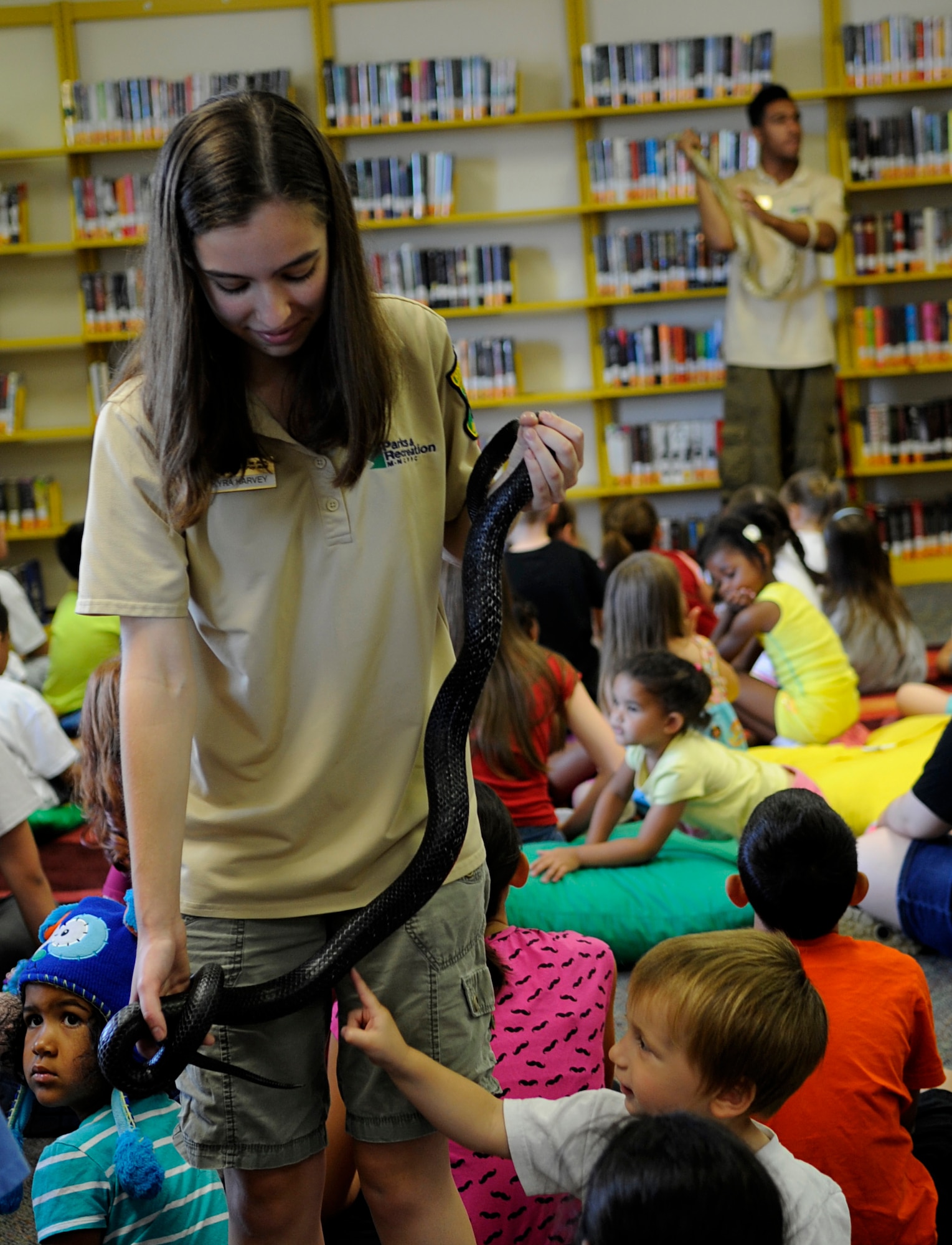 Kyra Harvey walks around with a black rat snake for children to pet at the library on Joint Base Andrews, Md., June 24, 2014. Harvey is a Cosca Regional Park’s Clearwater Nature Center naturalist, who taught JBA families about a variety of reptiles’ behaviors, habitats and anatomy. (U.S. Air Force photo/Senior Airman Nesha Humes)