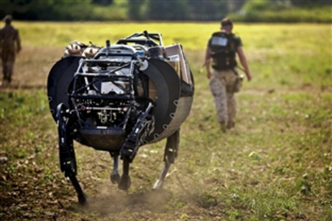 Marine Corps Lance Cpl. Timothy Knaggs, center, walks ahead of a legged support system at Marine Corps Training Area Bellows on Oahu, Hawaii, June 19, 2014. The legged system is designed to carry supplies, including water, food and ammunition, through rough terrain.