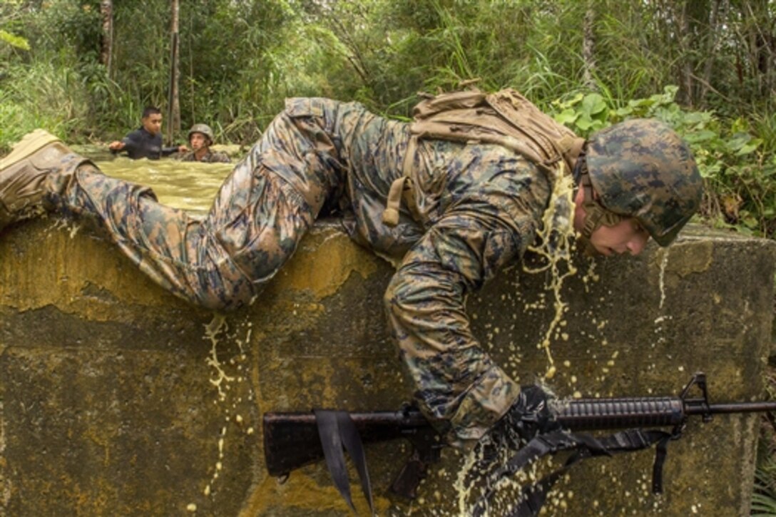 U.S. Marine Corps Cpl. Kevin E. Kusler maintains a low profile while he crawls over a stone wall during the jungle endurance course at the Jungle Warfare Training Center on Camp Gonsalves in Okinawa, Japan, June 20, 2014. Kusler, a machine gunner, is assigned to 1st Battalion, 8th Marine Regiment, 4th Marines, 3rd Marine Division, III Marine Expeditionary Force. 