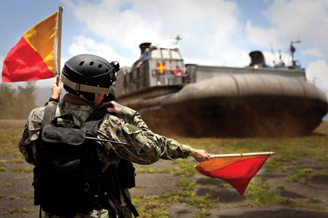 Sailors with Beach Master Unit 1, guide to sea Landing Craft Air Cushion vehicles assigned to Assault Craft Unit 5, at Hale Koa Beach, Marine Corps Base Hawaii, June 25, 2014. The hovercraft were used to load vehicles from 3rd Marine Regiment and Combat Logistics Battalion 3 onto amphibious assault ships USS Peleliu and USS Rushmore in support of Exercise Rim of the Pacific 2014. (U.S. Marine Corps photo by Cpl. Matthew Callahan)