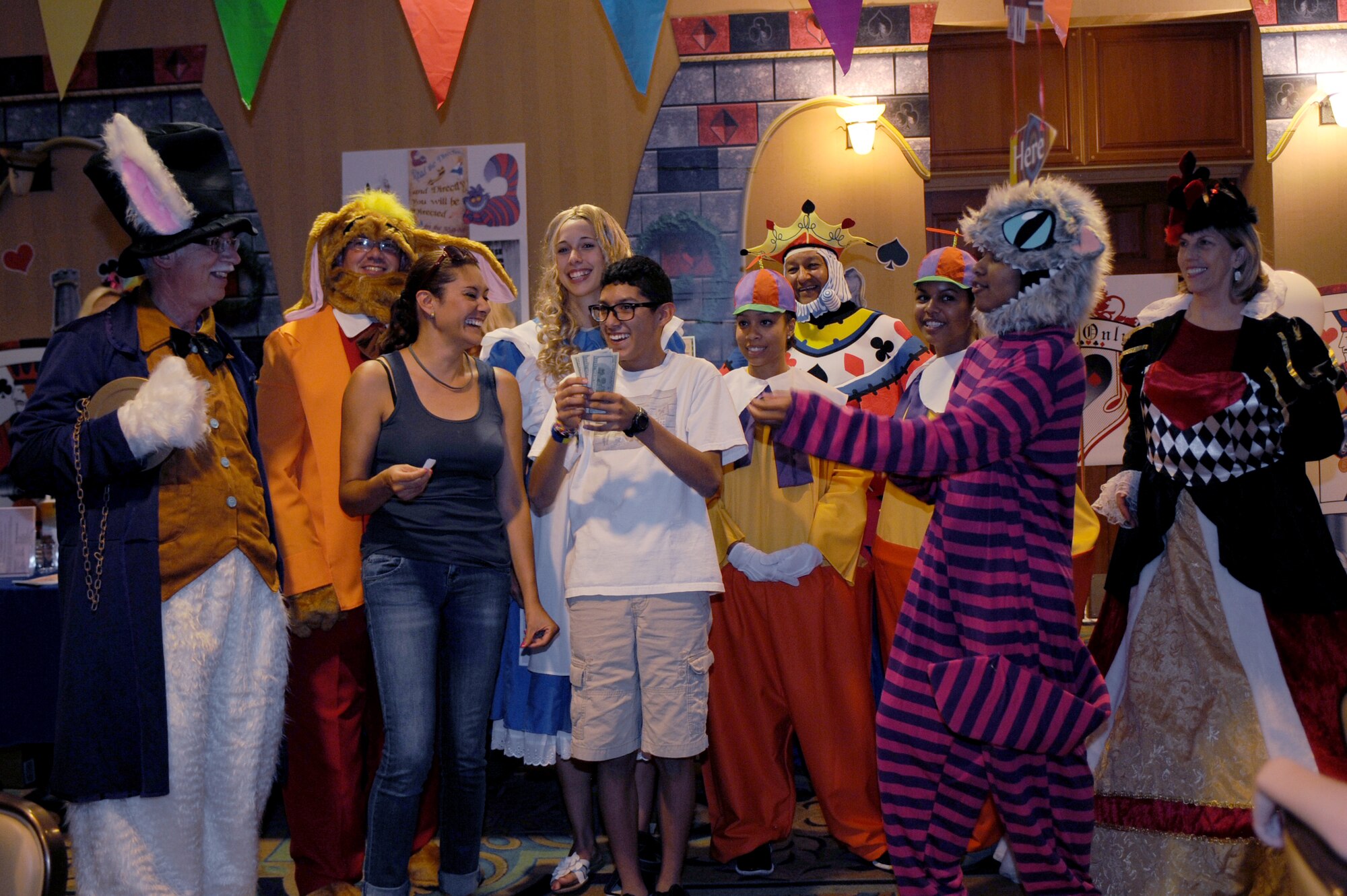 Two Desert Lightning Team members celebrate winning the grand prize with the characters from Alice in Wonderland during the “Meet Force Support Squadron Unbirthday Celebration” at Davis-Monthan Air Force Base, Ariz., June 26, 2014. During the event, different facilities handed out tickets to participants who visited their displays for a chance to win door prizes. (U.S. Air Force photo by Airman 1st Class Cheyenne Morigeau/Released)