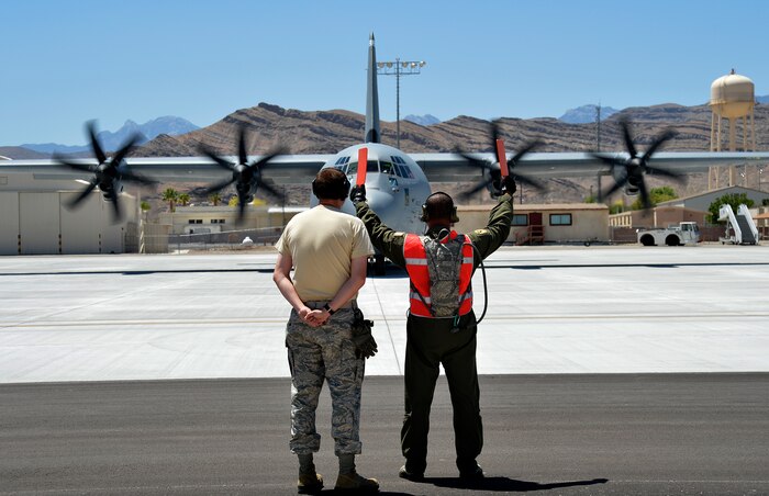 Tech. Sgt. Segric Hayes, right, from the 818th Global Mobility Squadron, McGuire Air Force Base, N.J., marshals a C-130J Super Hercules aircraft as it prepares to take off from Creech AFB, Nev., June 22, 2014.  Hayes and other 818th CRG Airmen, along with C-130H and C-130J model aircraft from various units, participated in Joint Forcible Entry, an exercise that helps Army and Air Force improve services cohesiveness and  work together to properly execute large scale heavy equipment and troop movement. (U.S. Air Force photo by 1st Lt. Stephani Schafer/Released)